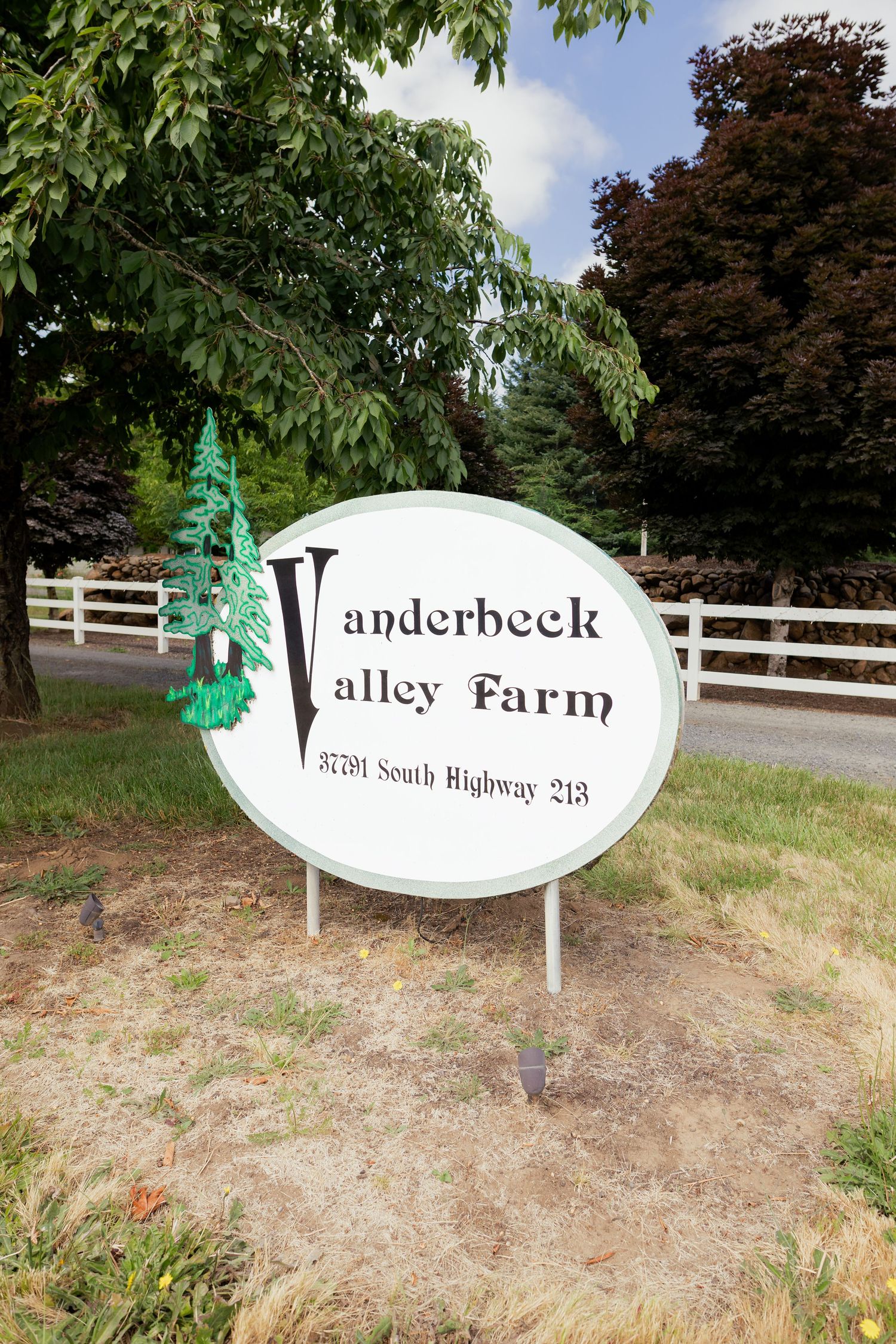 Vanderbeck Valley Farm sign at 37791 South Highway 213 surrounded by lush green trees and white fence.