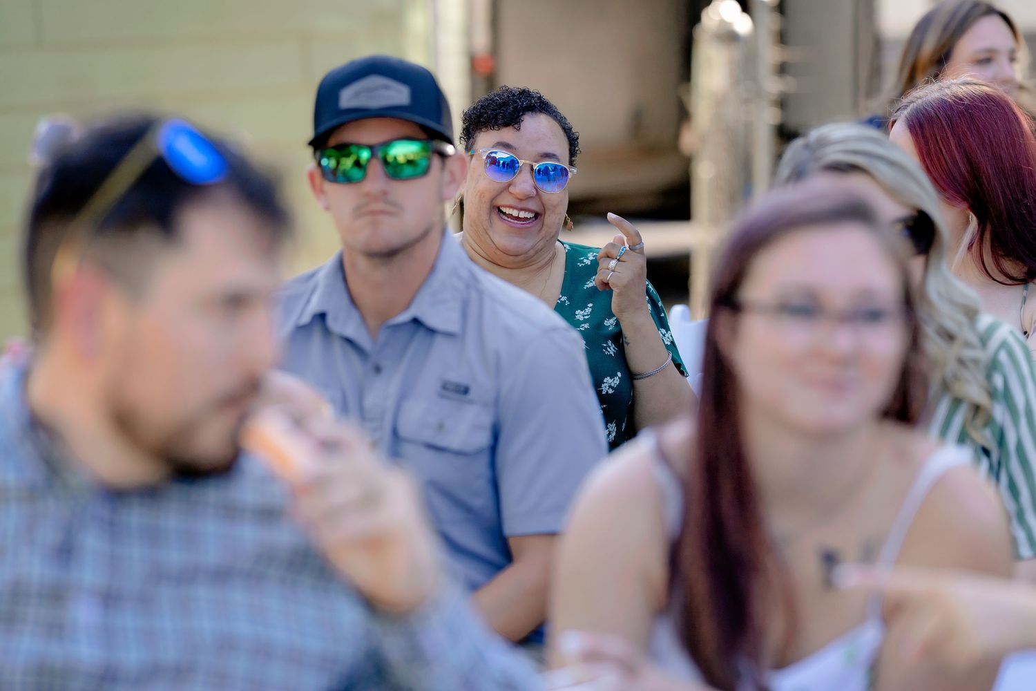Group of young adults wearing sunglasses socializing outdoors at a sunny event, smiling and enjoying the gathering.