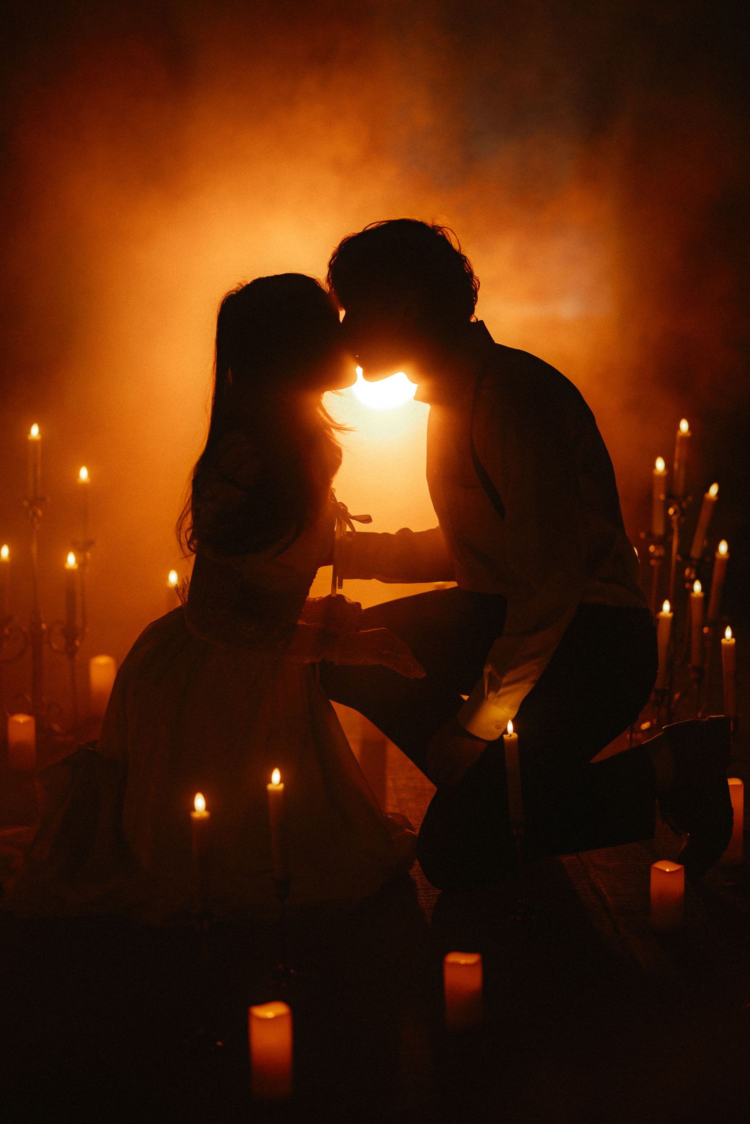 Silhouettes of people illuminated by candlelight in a dark atmospheric setting.