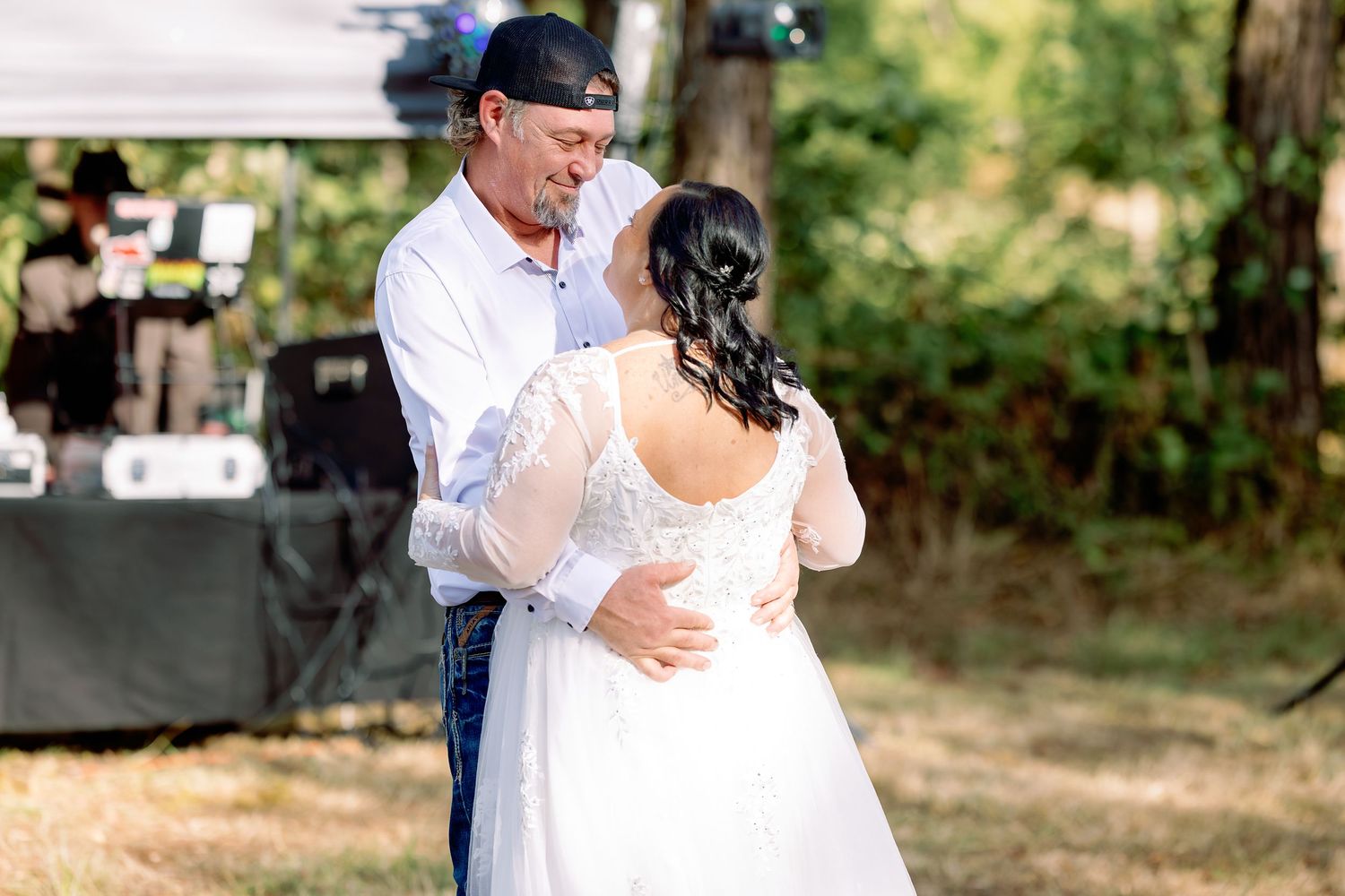 A couple shares their first dance at an outdoor wedding reception surrounded by trees and natural light.