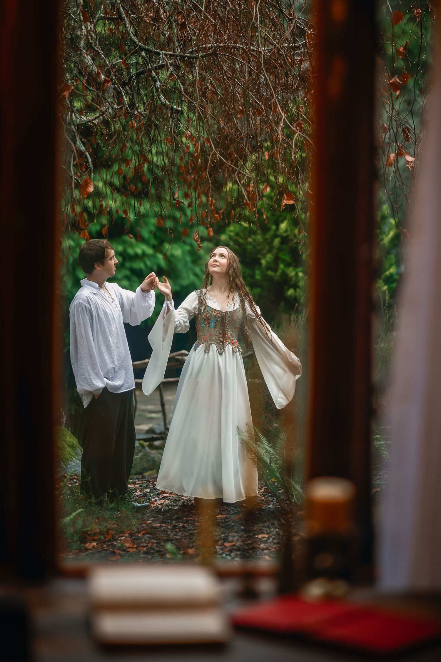 People in vintage-style clothing dance in a garden setting viewed through window frames.