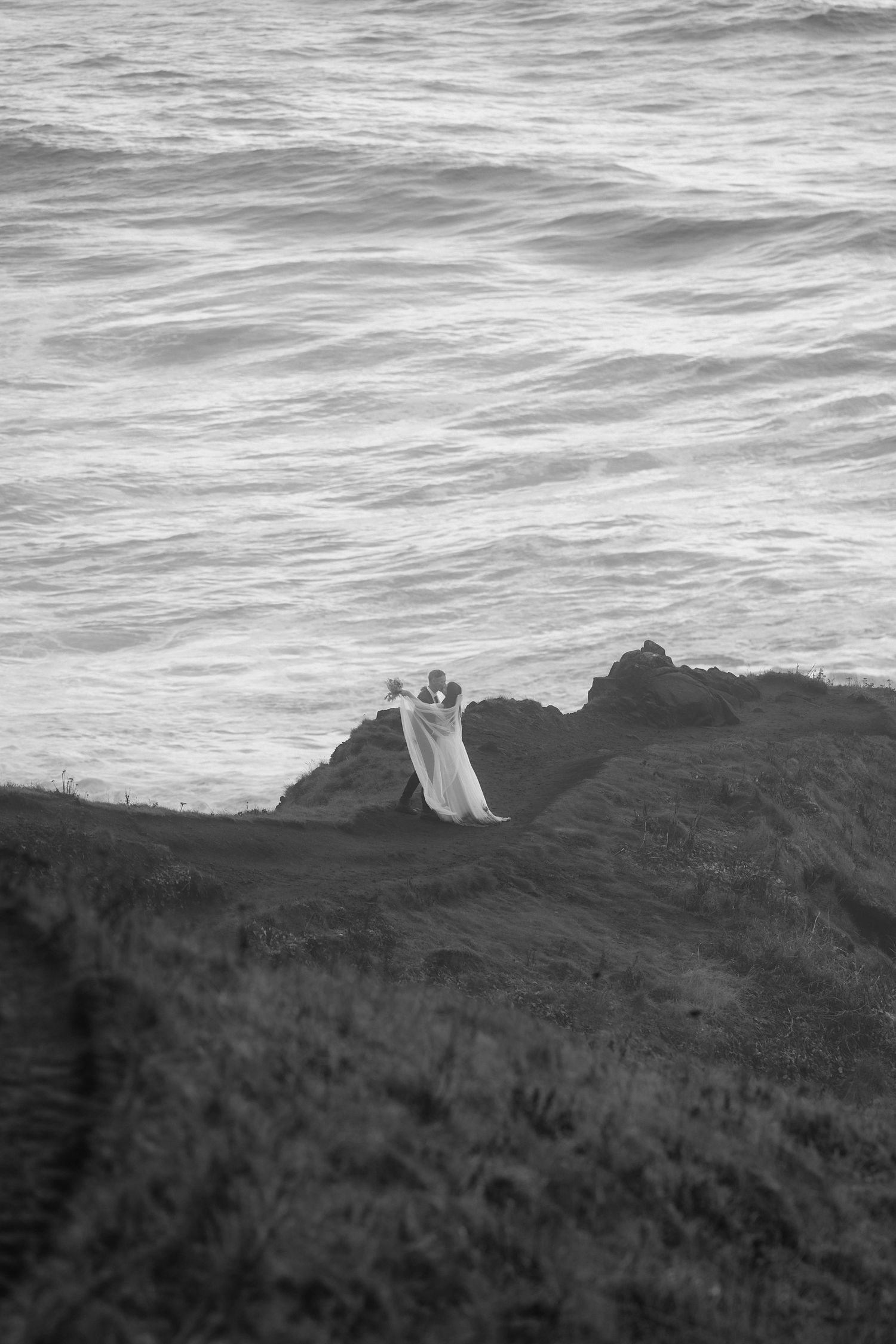 A series of black and white coastal landscape photos showing waves crashing against dark cliffs with a small structure visible.