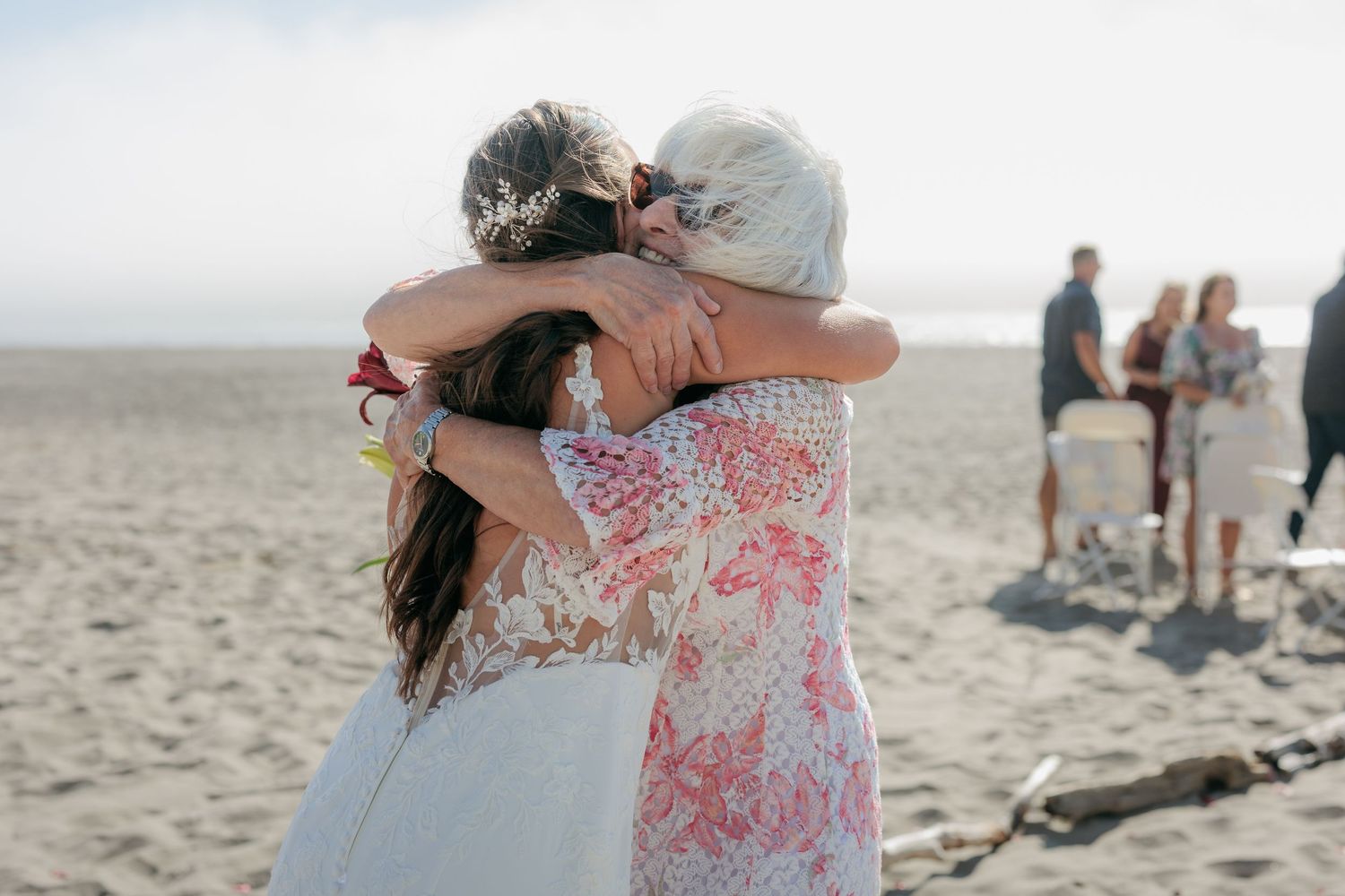 Romantic moments captured on a beach with guests in the background.