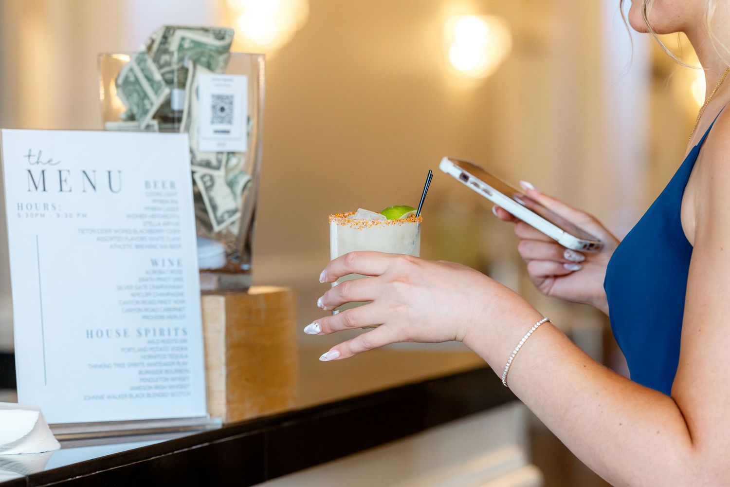 Wedding guest photographs cocktail hour drink menu with smartphone at the bar.