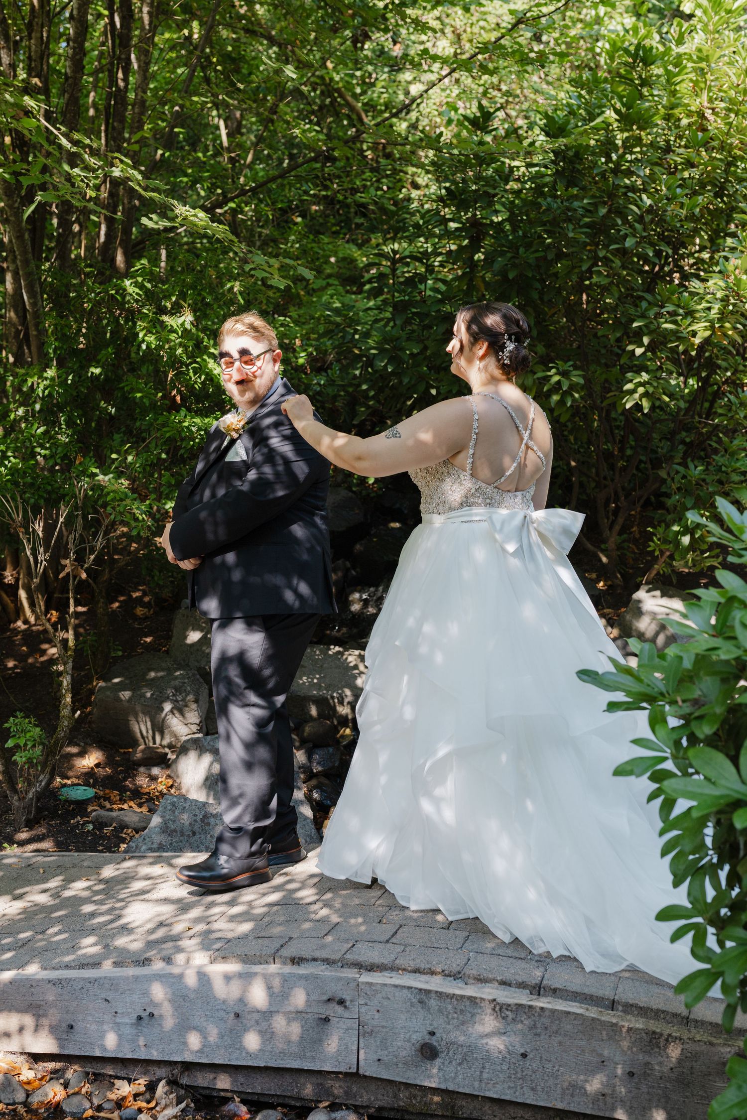 Bride in a white ballgown tapping groom on shoulder during an emotional first look in a garden.