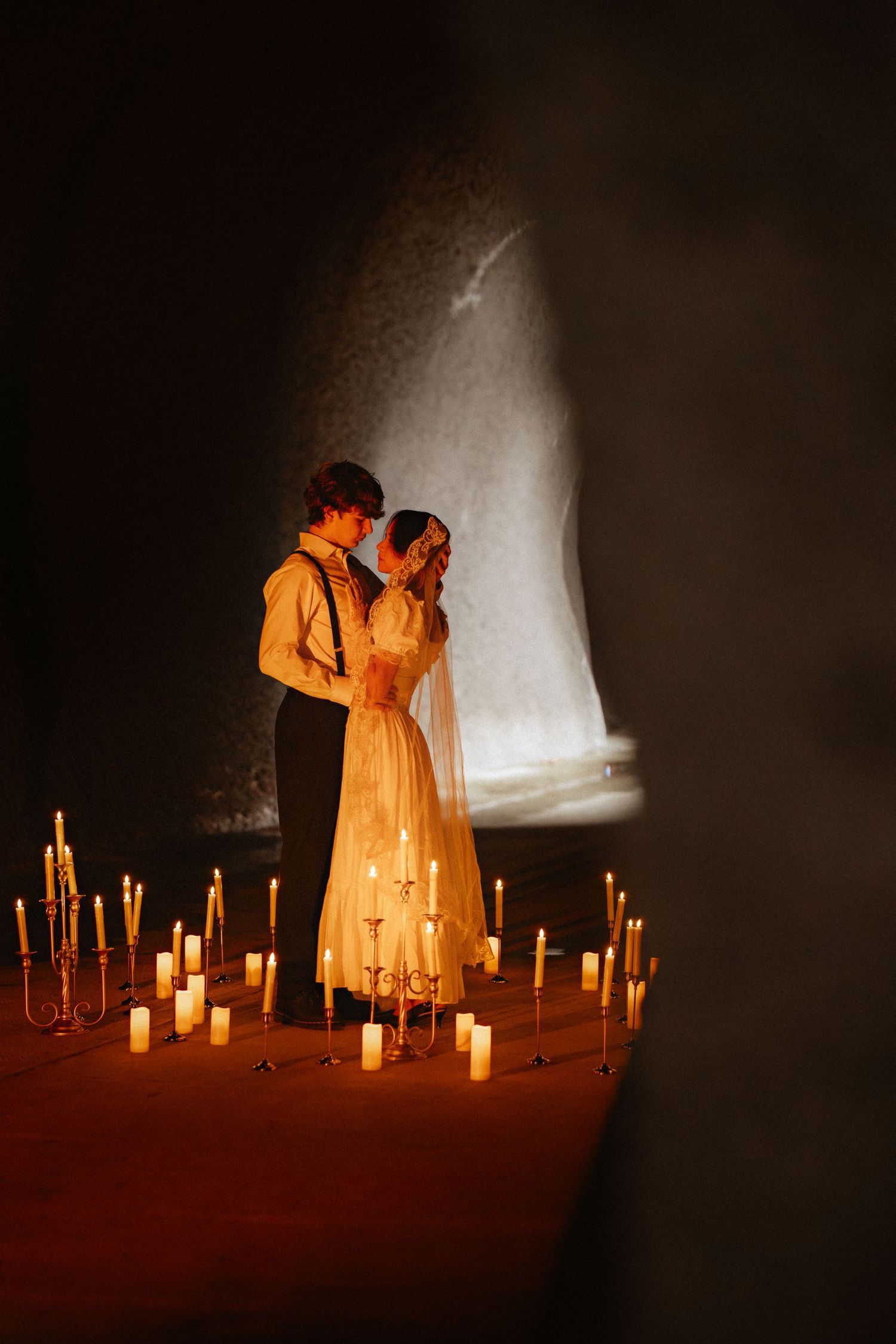 A couple in vintage clothing share an intimate moment surrounded by glowing candlelight.