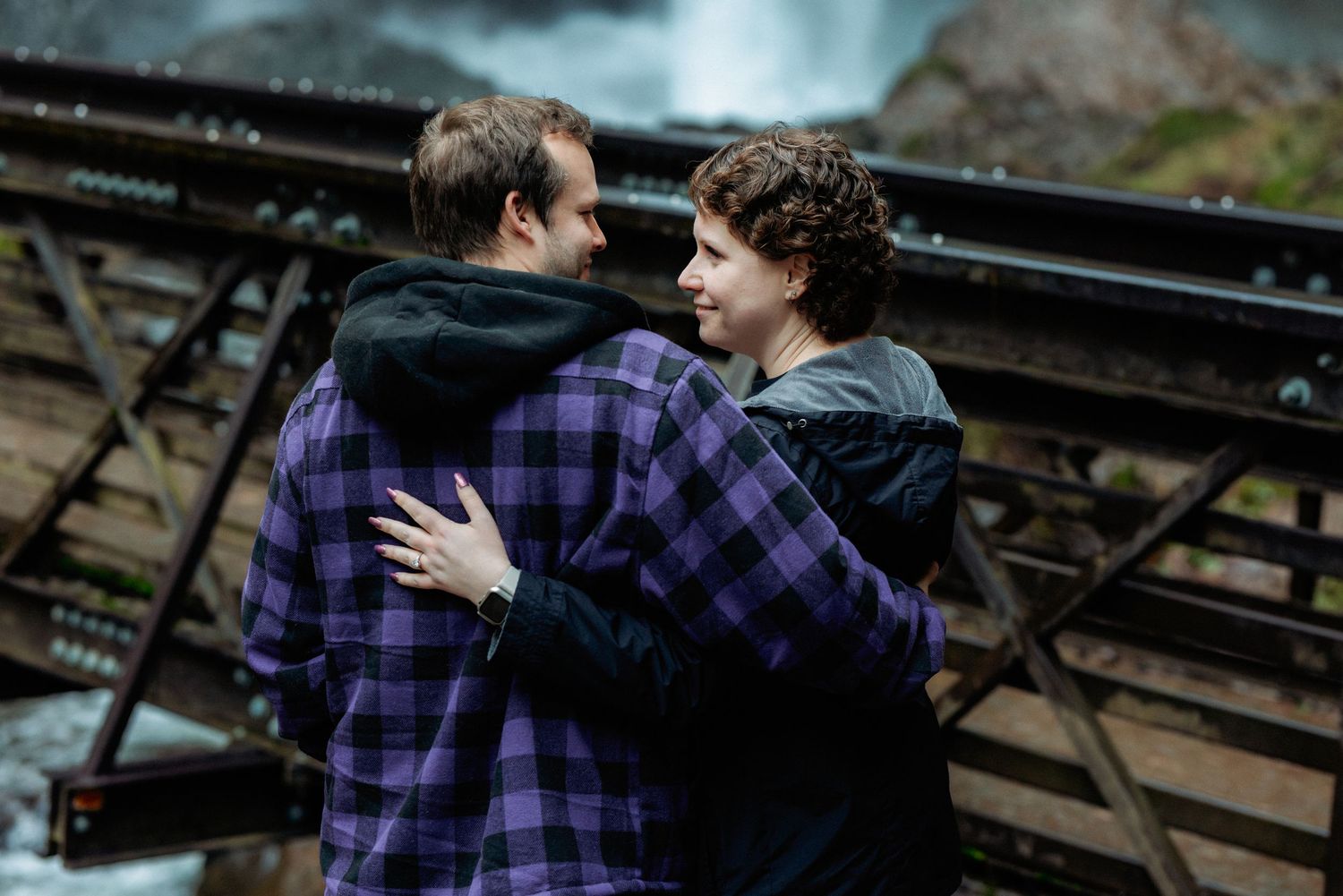 Two people in purple plaid shirts embrace and share a tender moment on wooden bleachers.