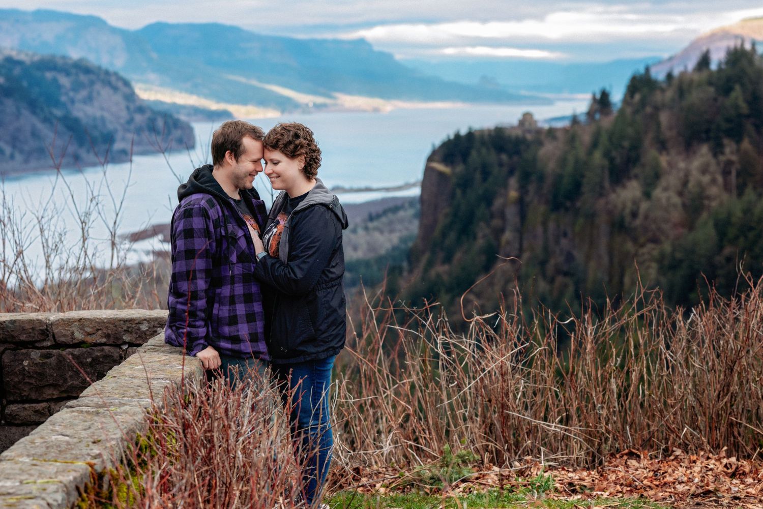 Two people embrace against a scenic backdrop of mountains and water at Columbia River Gorge in Oregon.
