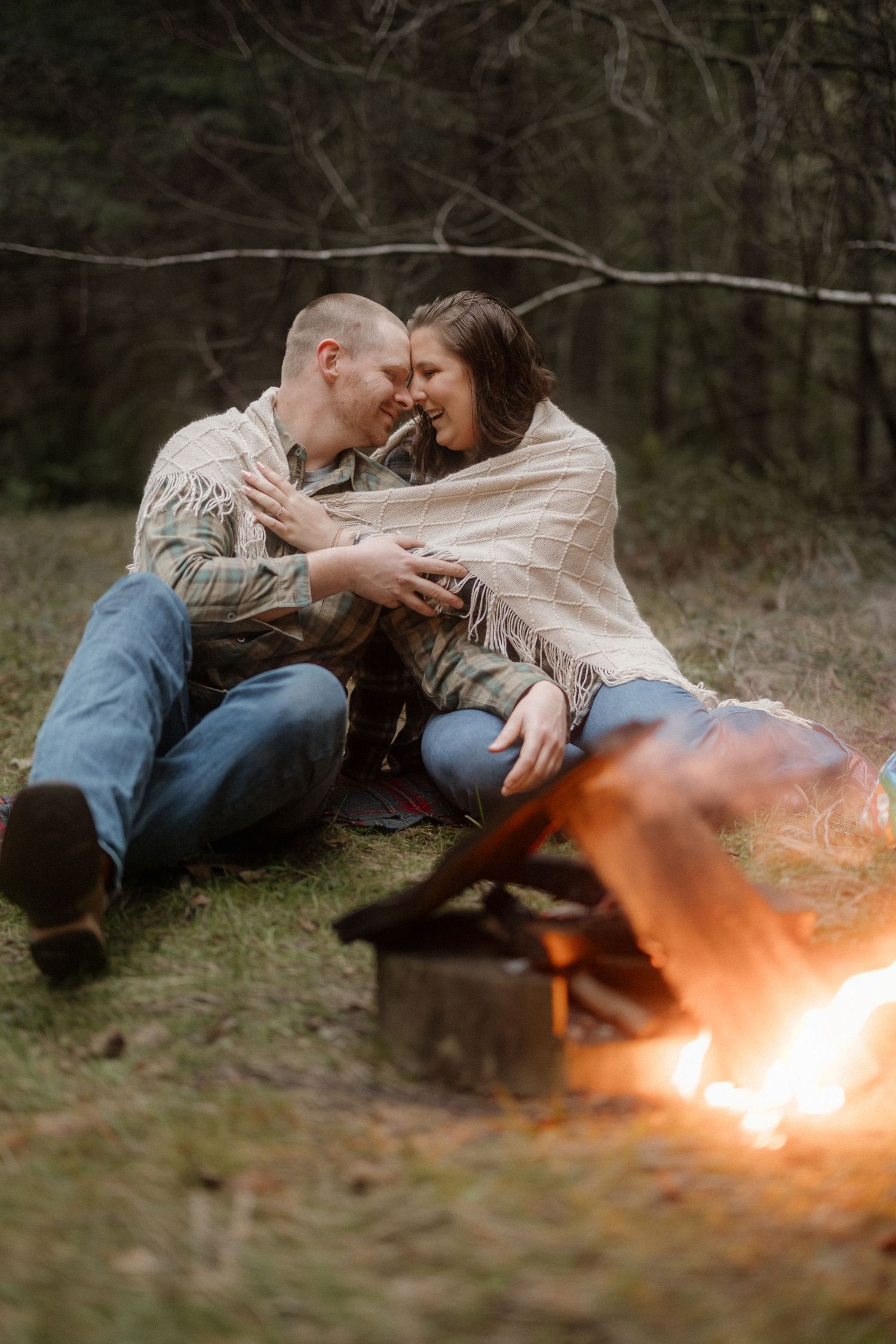 Romantic couple lying on grass with glowing fire effect in moody forest setting.