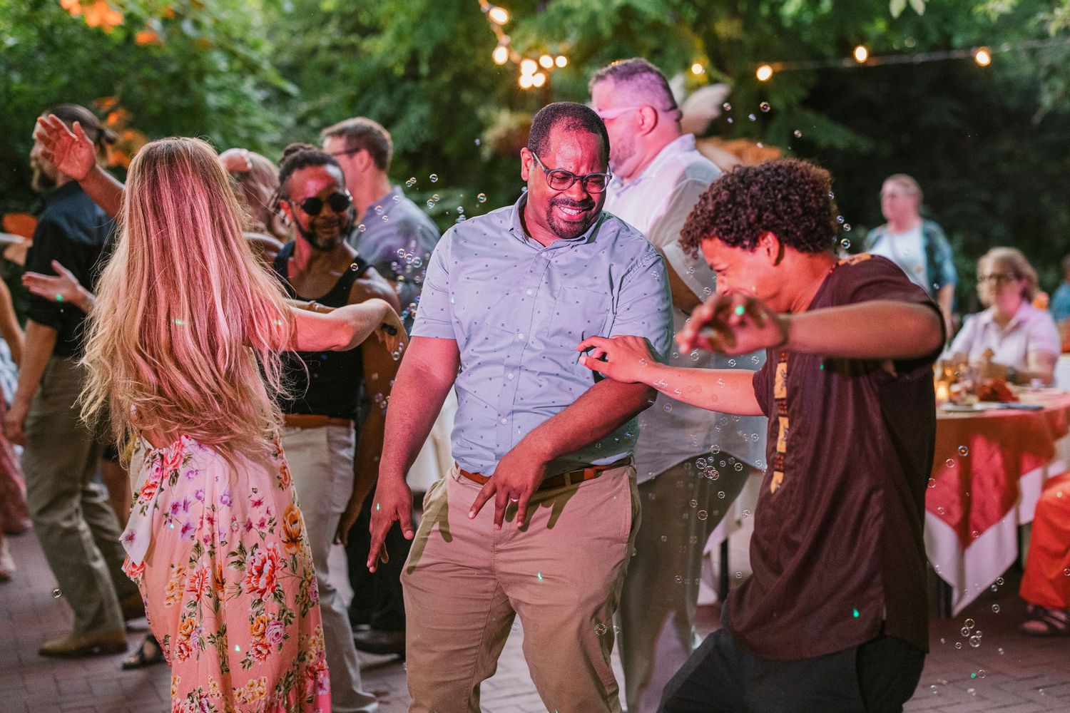 People dancing and having fun at an outdoor party with string lights in the background.