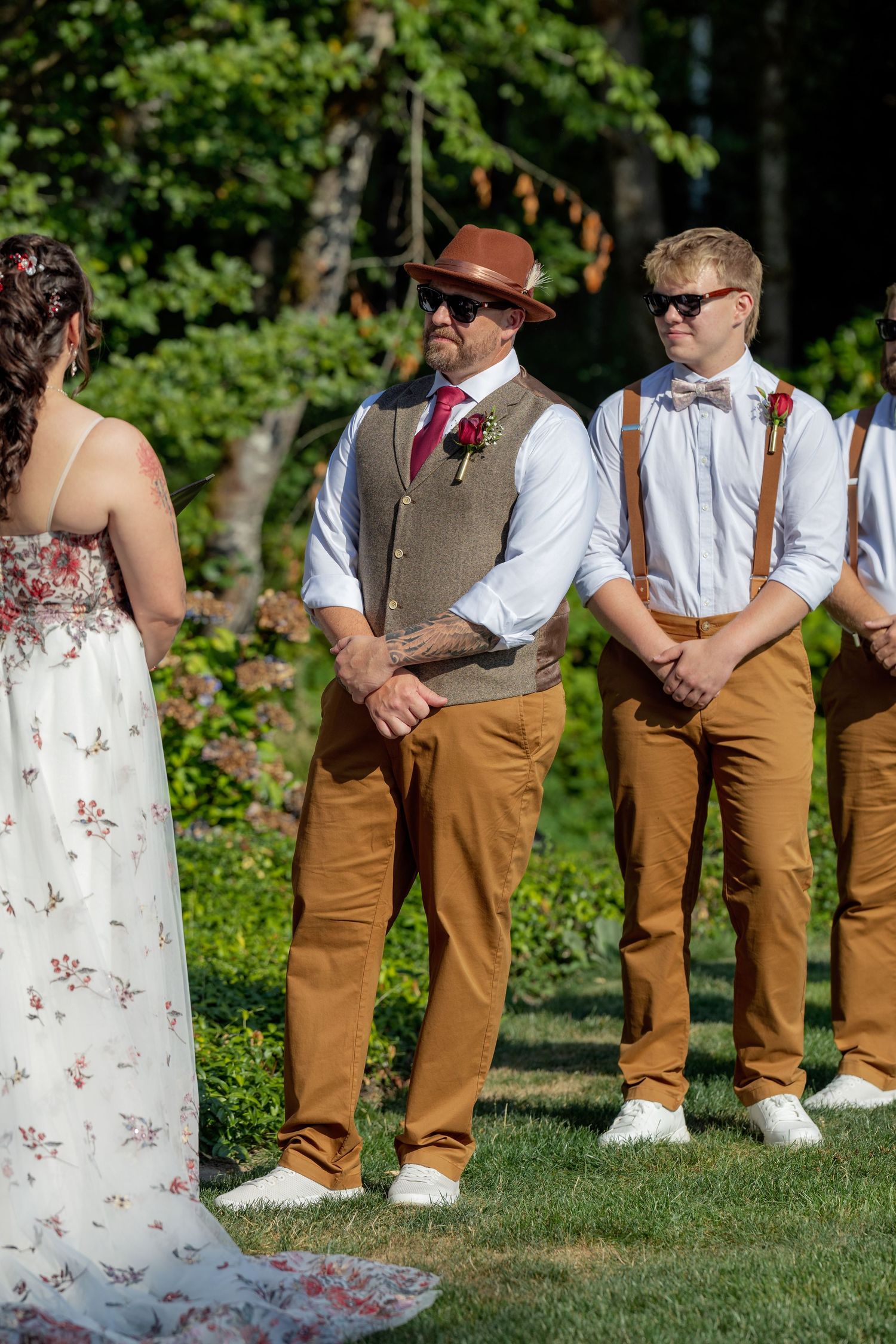 Wedding party lineup showing coordinated brown pants and white shirts against a garden backdrop.
