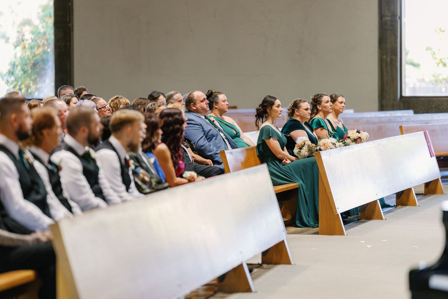 Side view of wedding guests seated in church pews during a ceremony.