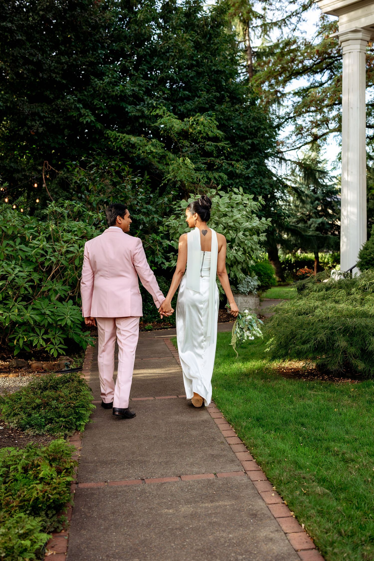 Couple walking hand in hand along a brick-lined path in formal wedding attire.