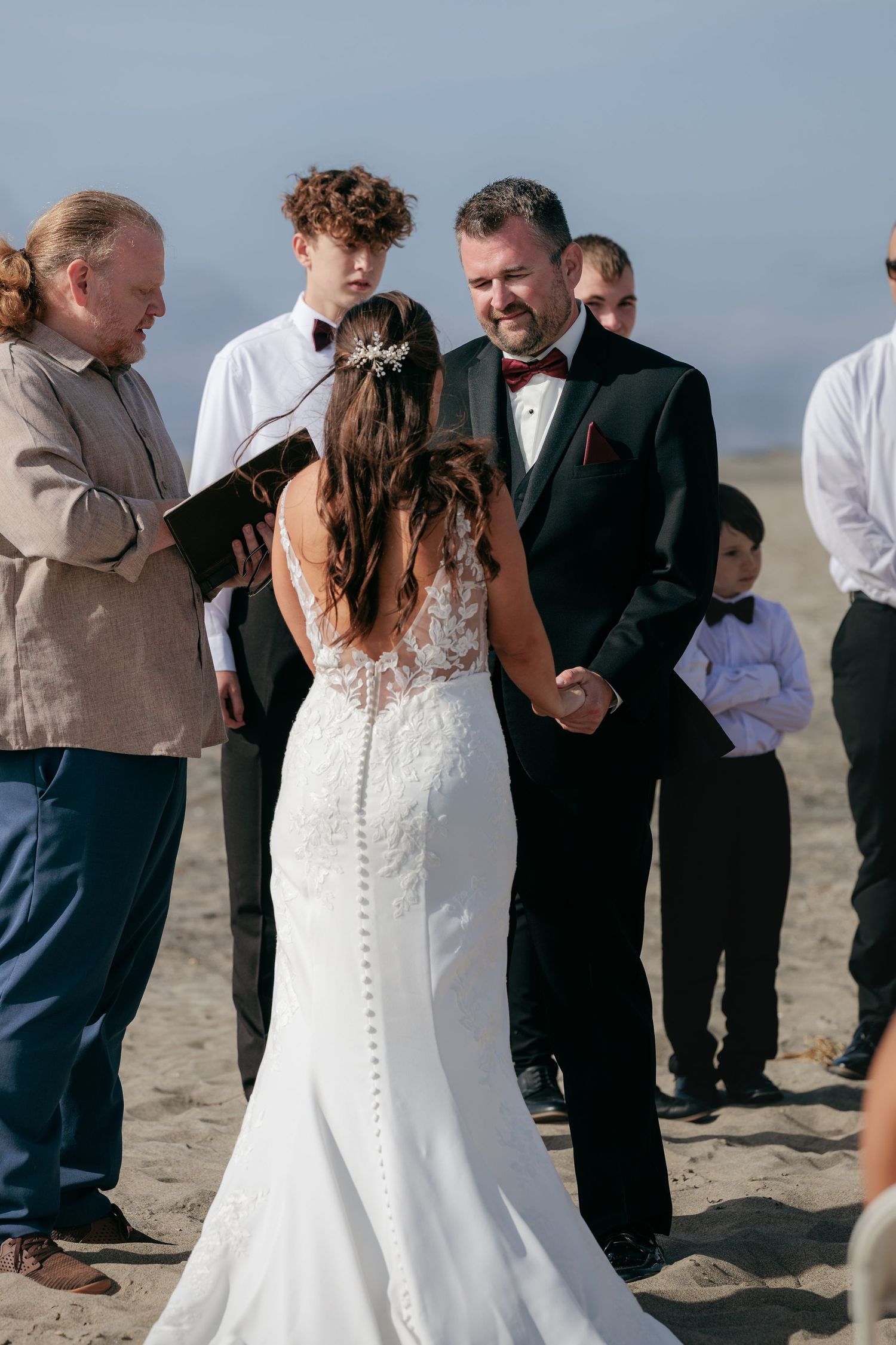 Outdoor beach wedding ceremony with guests watching couple exchange vows.