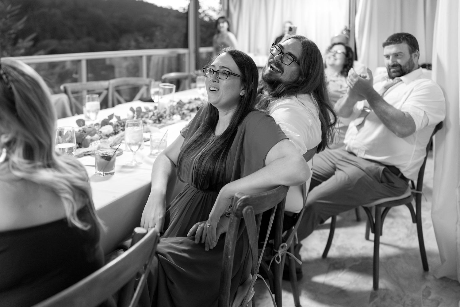 Group of wedding guests relaxing and laughing together on outdoor patio furniture.