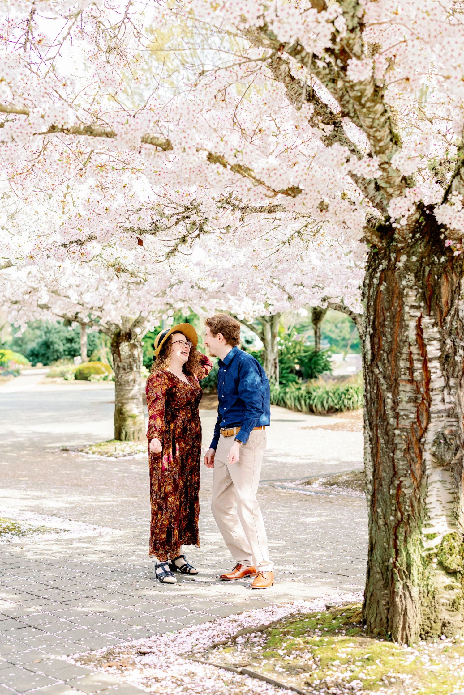 A couple shares tender moments under blooming cherry blossom trees in a park setting.