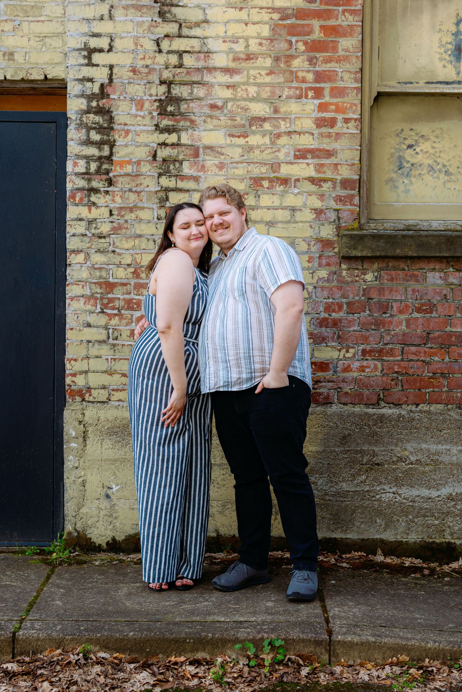 Couple in coordinating striped outfits posing against rustic brick wall.