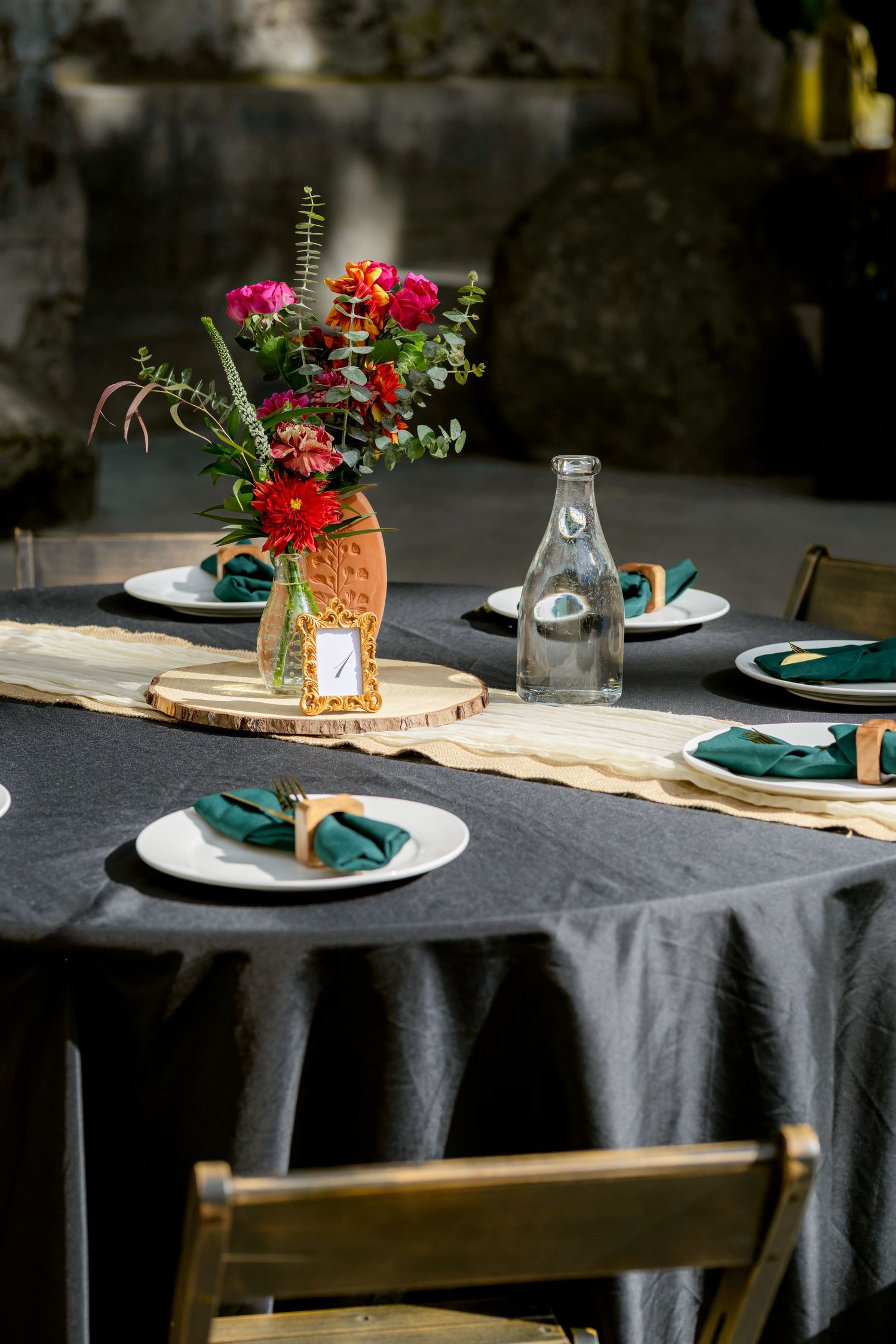 Elegant wedding reception table set with dark linen, green napkins, and vibrant floral centerpiece in terracotta vase.