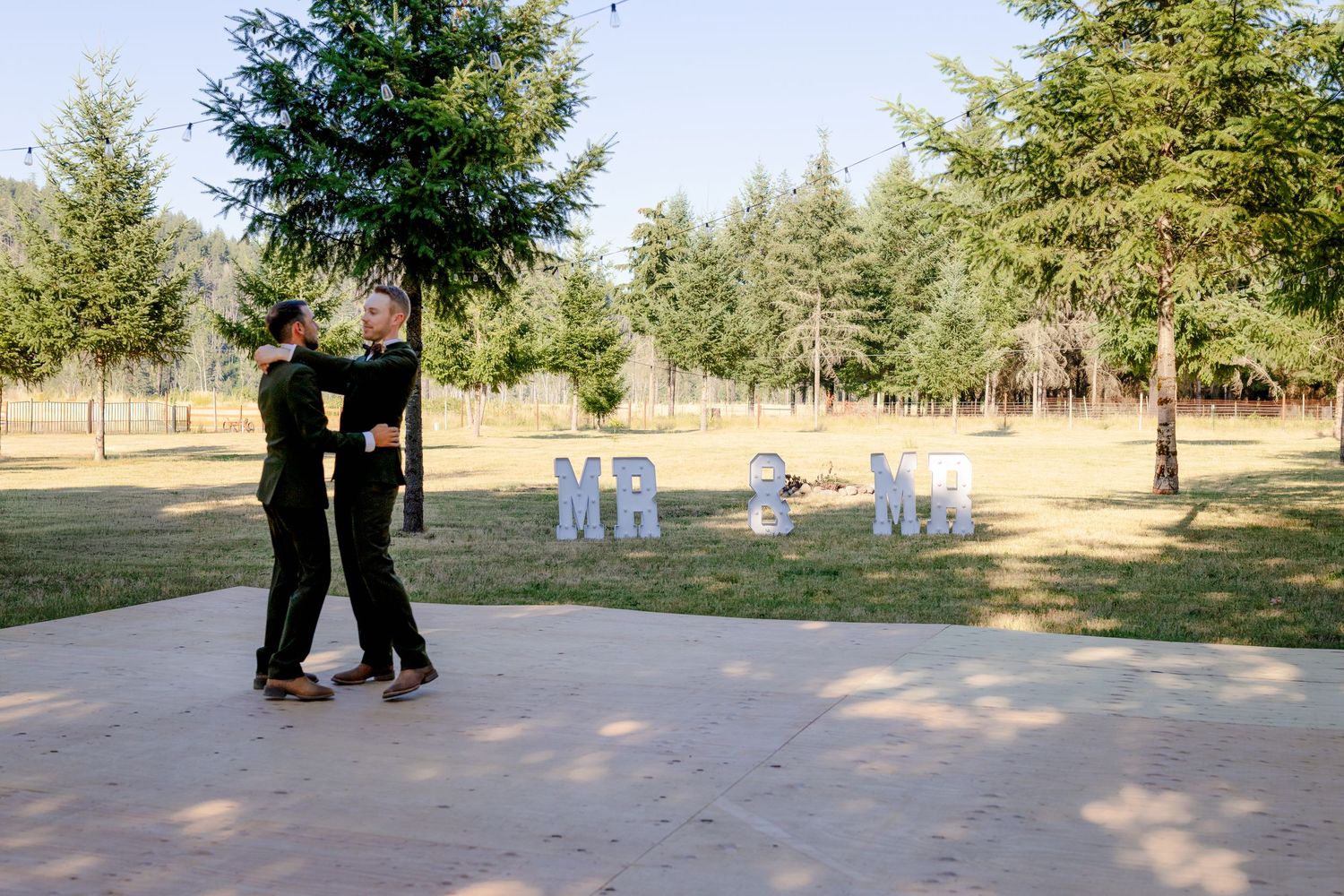 Couple shares first dance outdoors with marquee NR initials sign at rustic wedding reception.