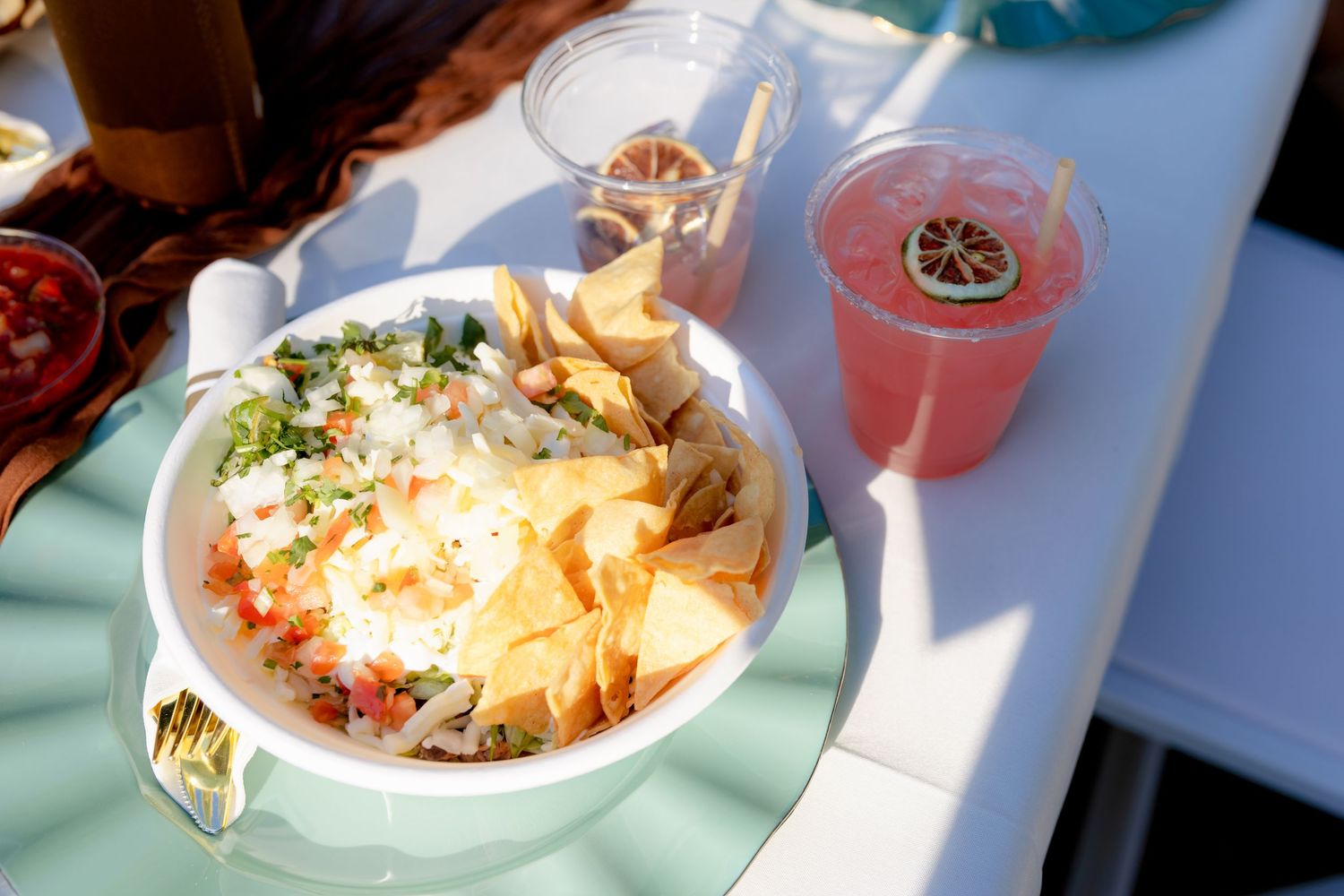 Outdoor wedding reception table with a bowl of nachos topped with cheese and guacamole beside a pink lemonade drink.