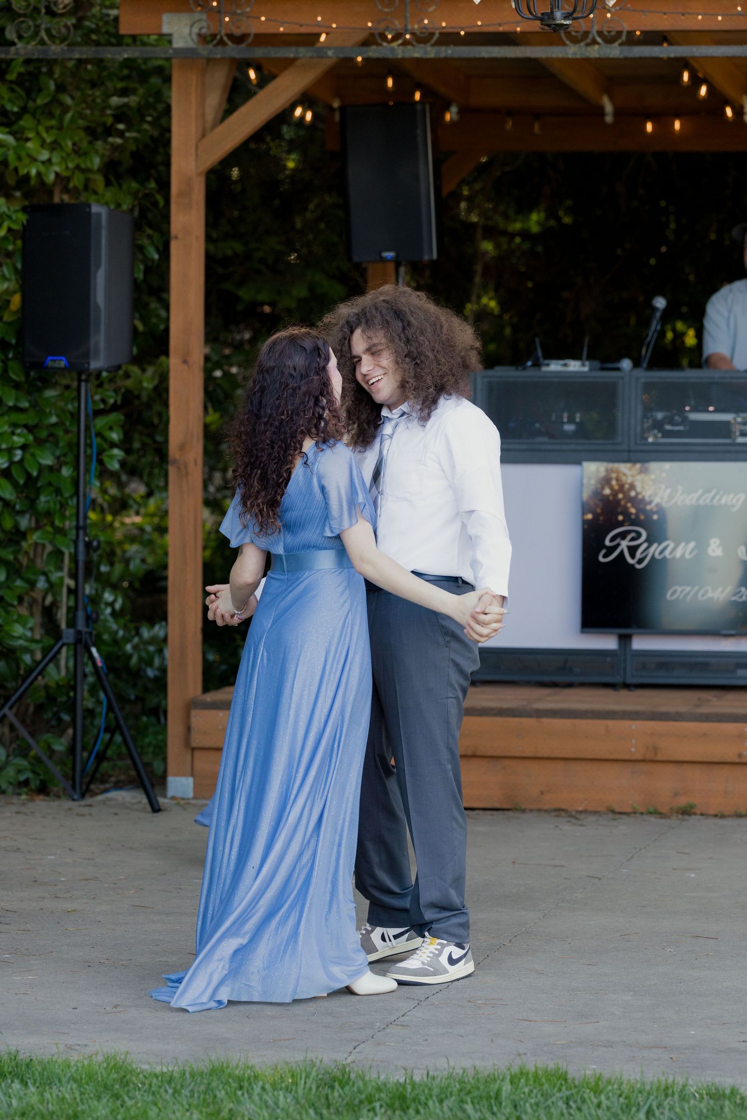 Couple sharing a romantic first dance outdoors at a wedding reception under string lights.