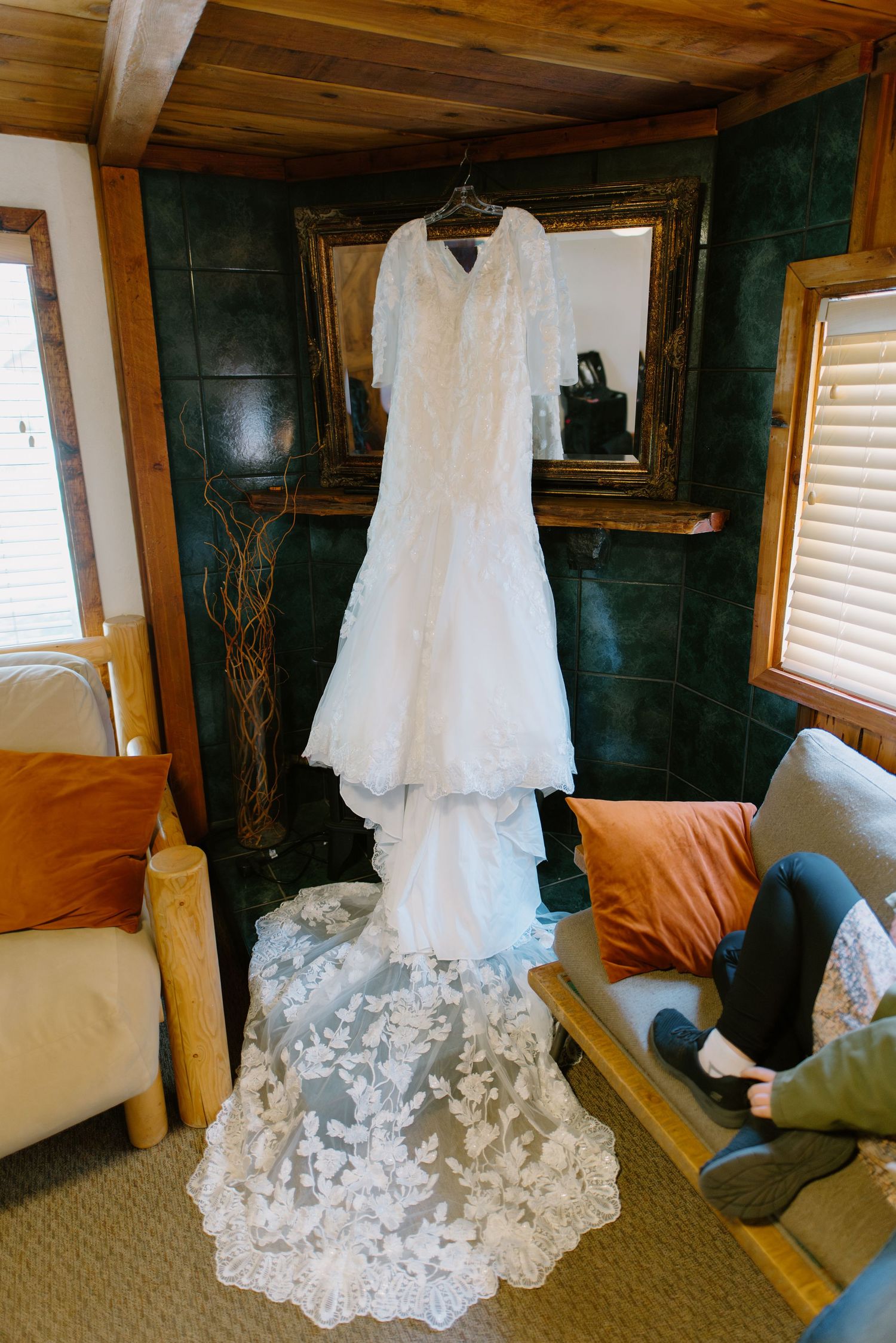 White lace wedding dress with floral train hanging in a rustic cabin room before the ceremony.
