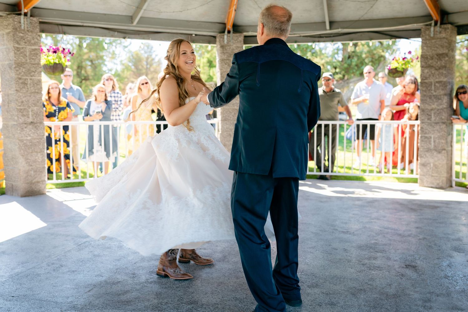 Bride and groom share their first dance under a pavilion surrounded by wedding guests.