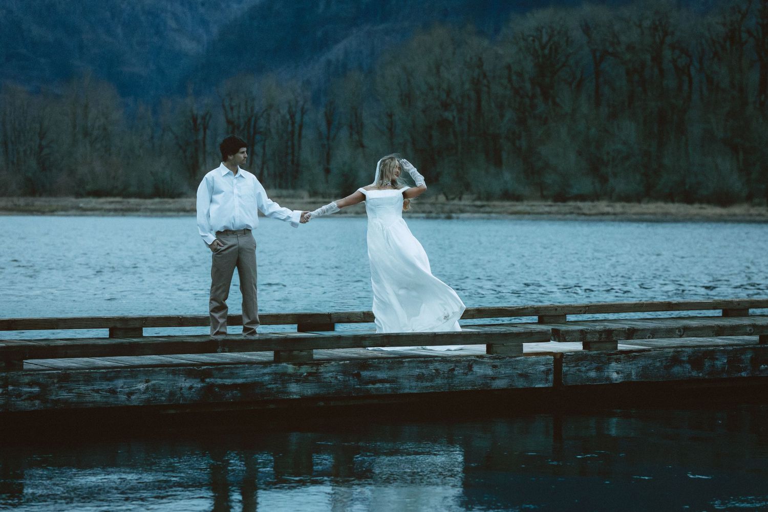 Wedding couple walking along a wooden dock with mountain lake views in the background.