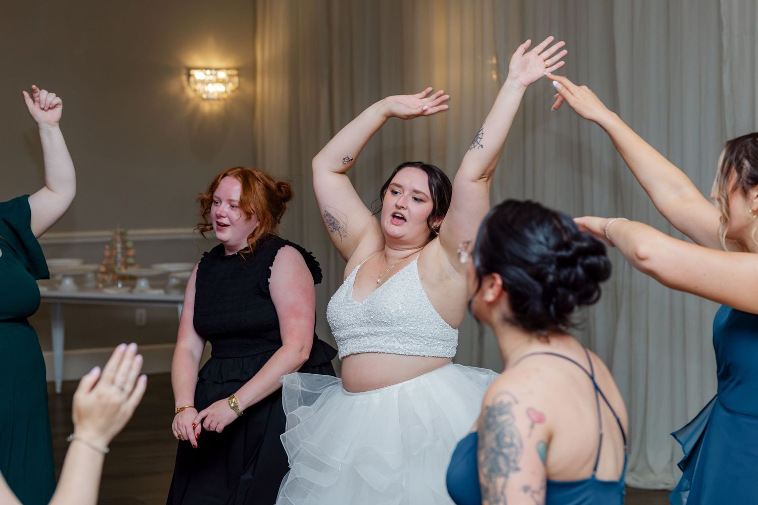 Bride dances joyfully with bridesmaids and guests on wedding reception dance floor.
