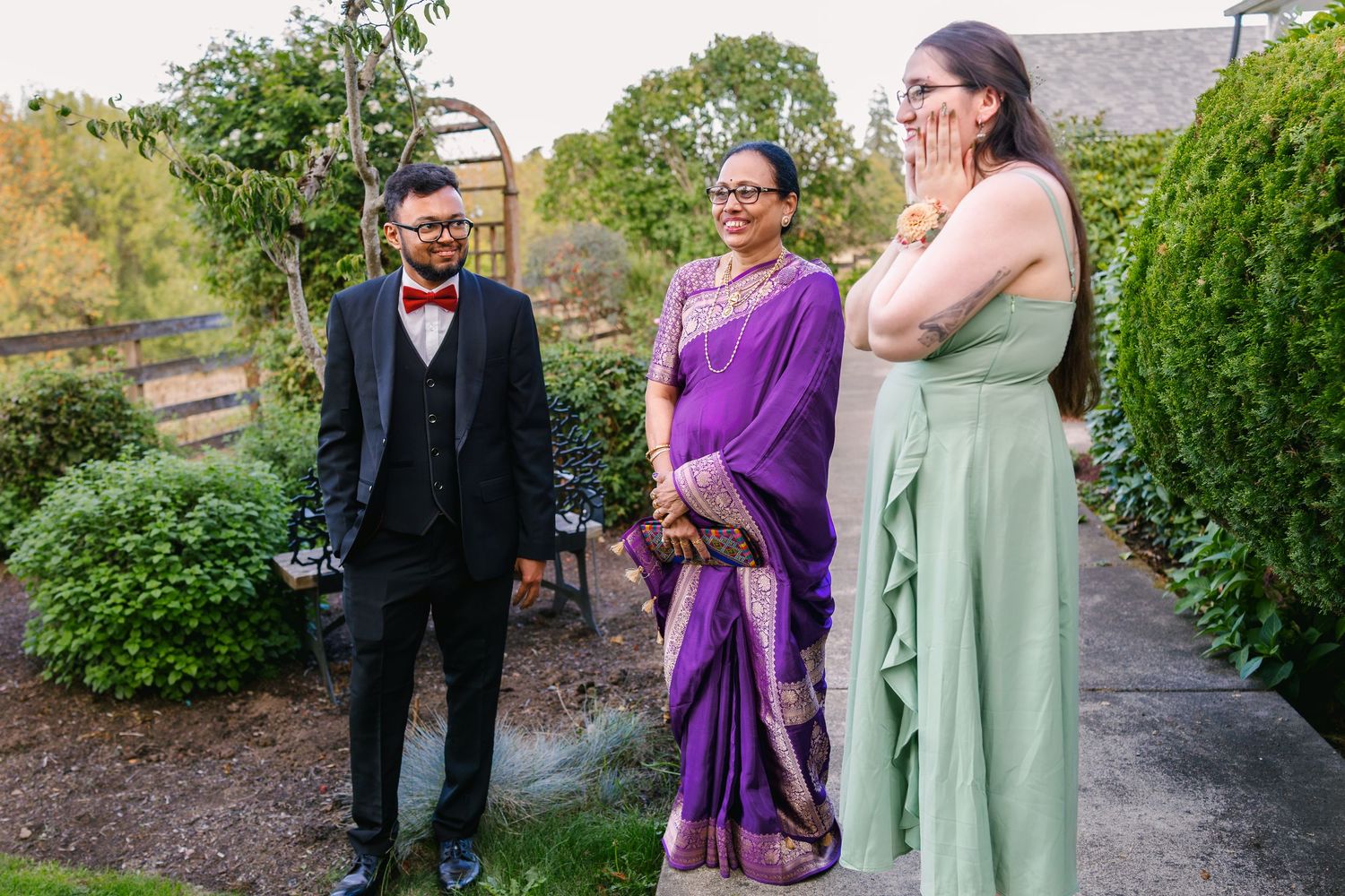 Three people share a joyful moment together outdoors, with one wearing a suit and another in a purple sari.
