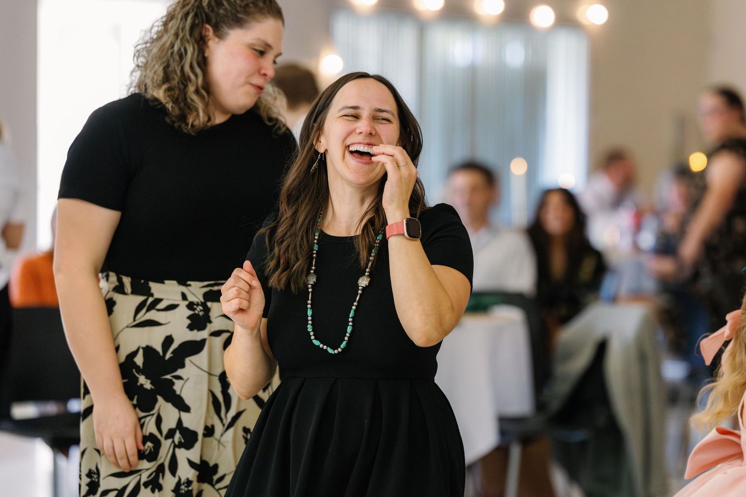 Wedding reception guests dance joyfully together under decorative lighting at an indoor venue.