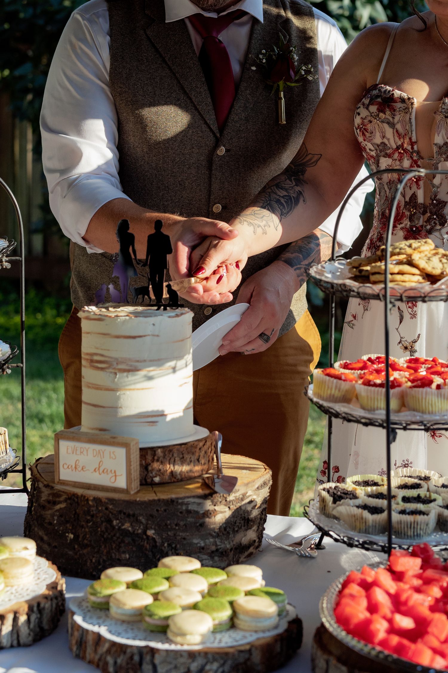 Wedding dessert table with cake and treats displayed on rustic wood slices with string lights in background.