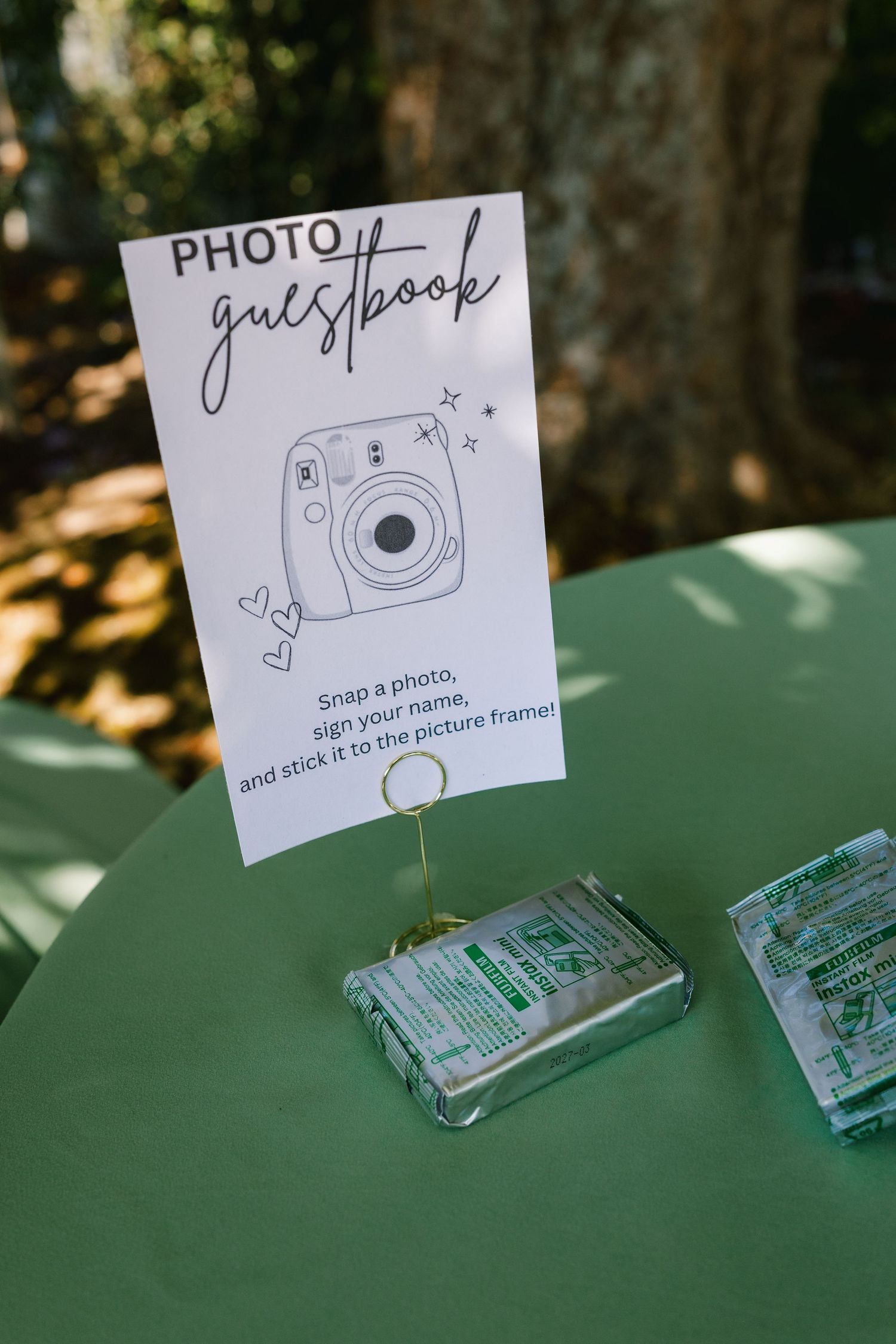 Guest book station with Instax camera instructions and supplies on a green table.