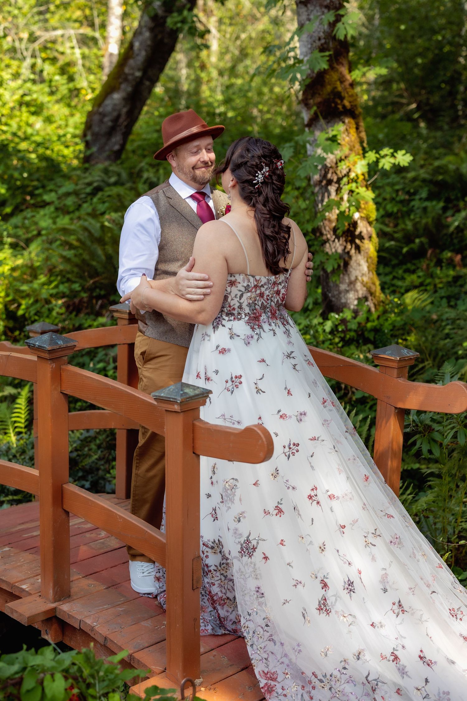 A romantic moment on a wooden bridge surrounded by lush green foliage in a garden setting.