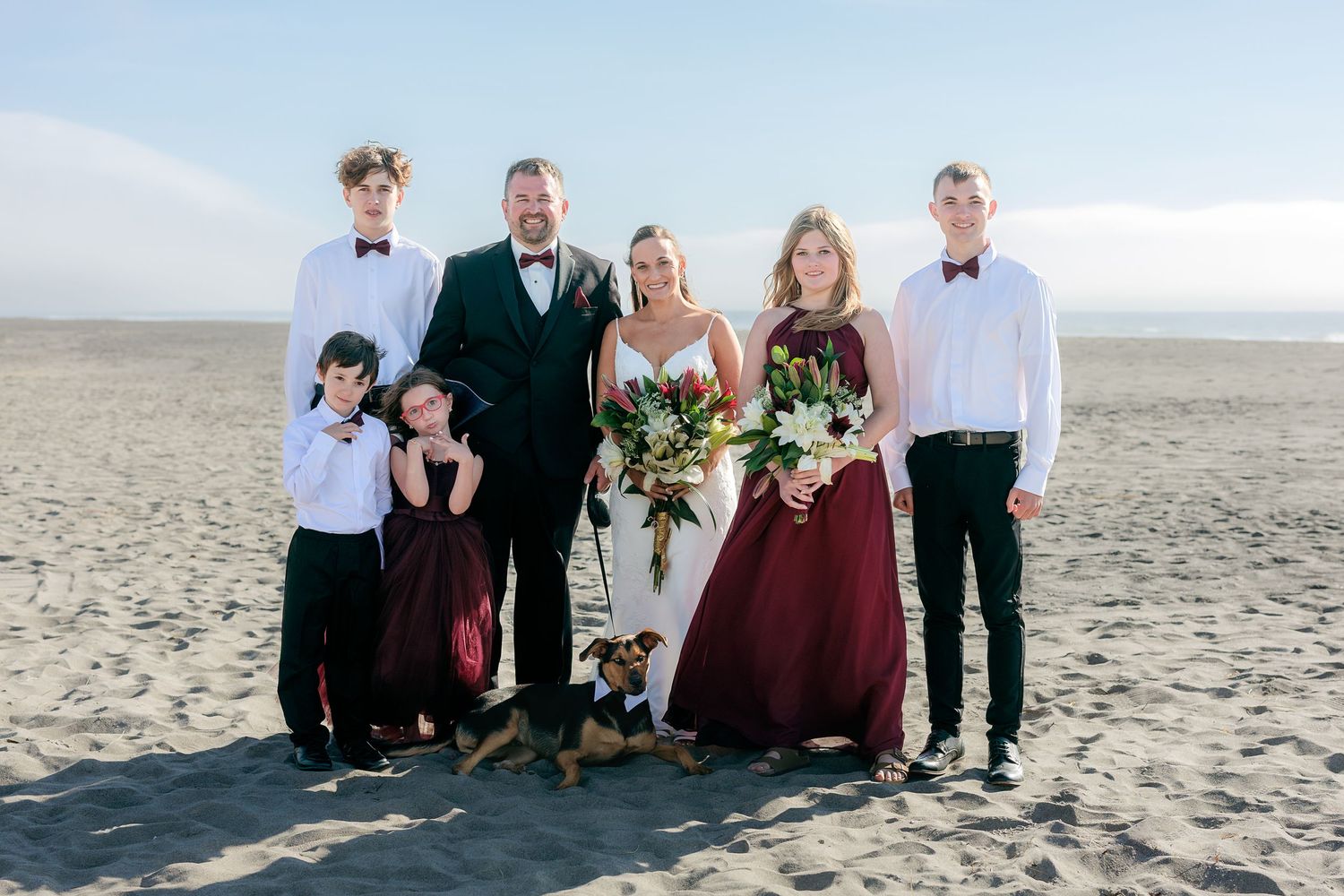Wedding group portrait on beach with burgundy and neutral color scheme.
