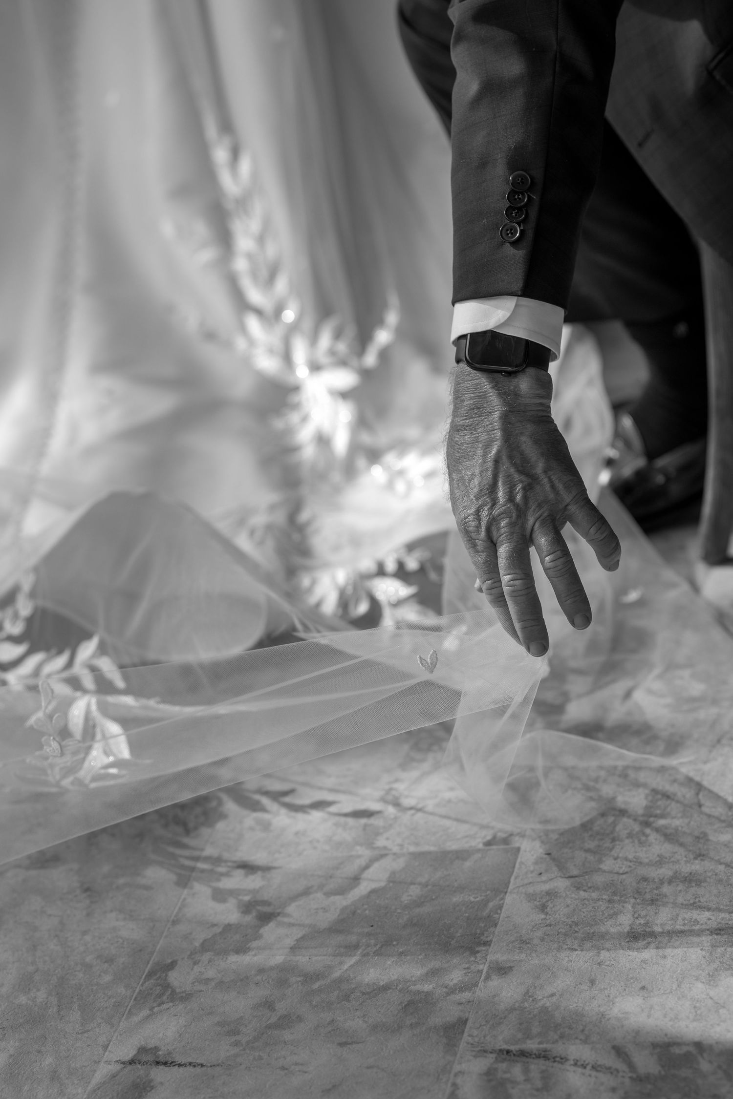 Close-up details of hands delicately touching flowing white fabric in black and white.