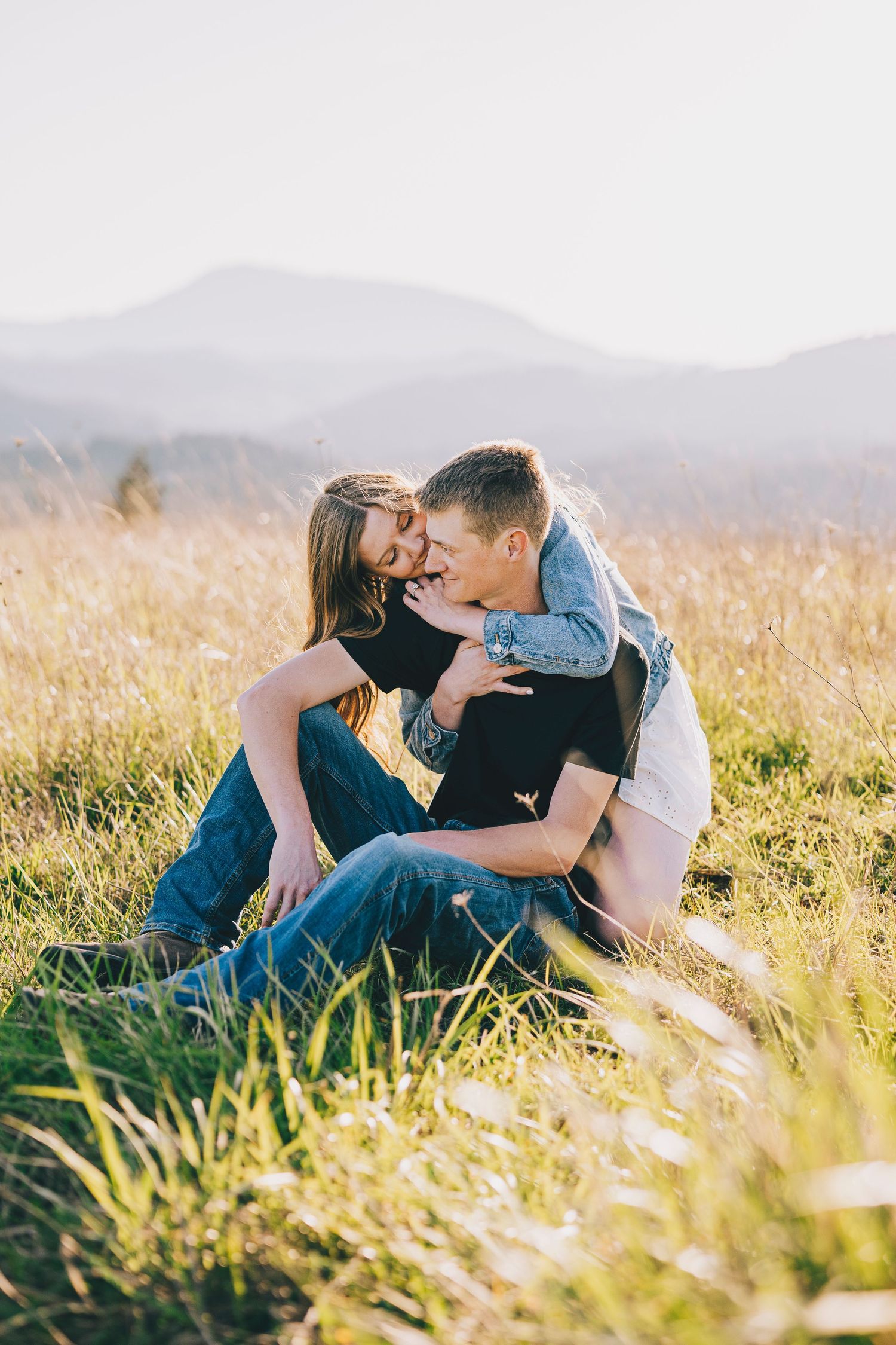 A romantic moment captured in tall grass with mountains in the distance during sunset.