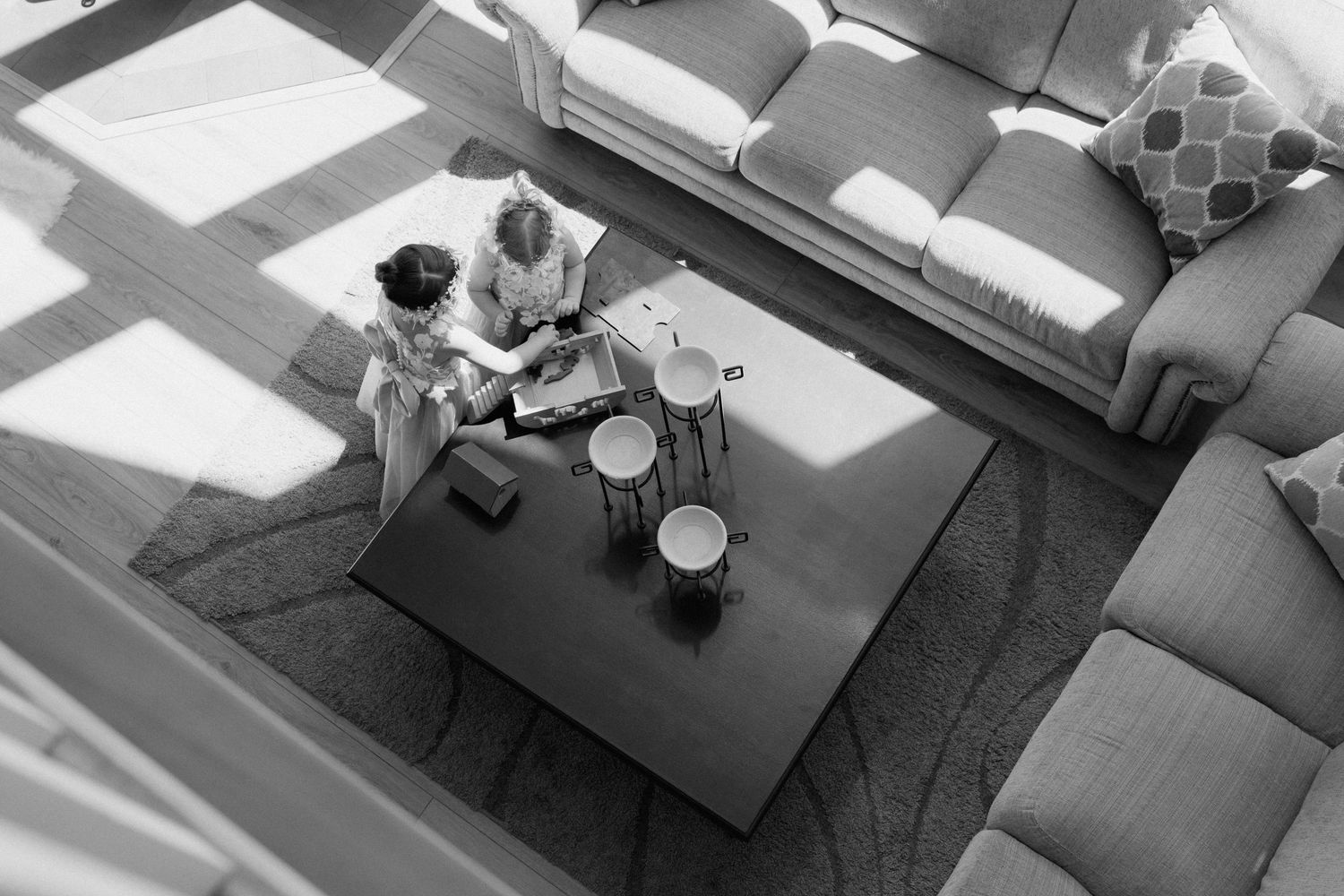 Aerial black and white photo of two people sitting together on a rug near a coffee table in a modern living room.