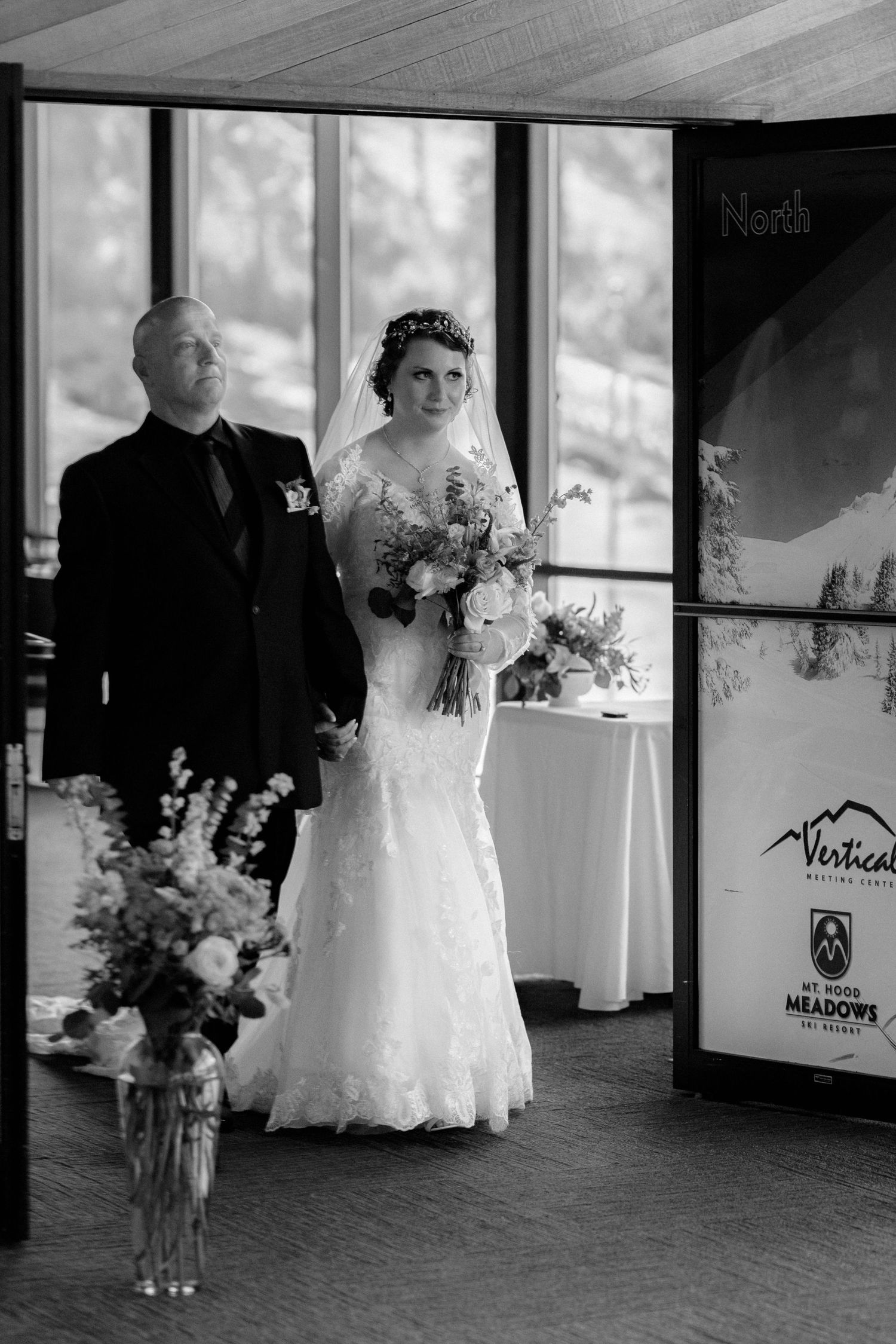 Bride in lace wedding gown holding bouquet walks down aisle with escort at Mt Hood Meadows wedding venue.