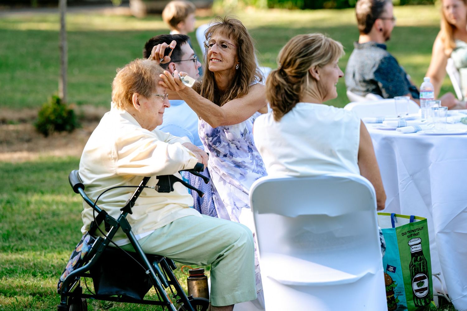 Wedding guests laugh and interact at outdoor reception tables on a sunny green lawn.
