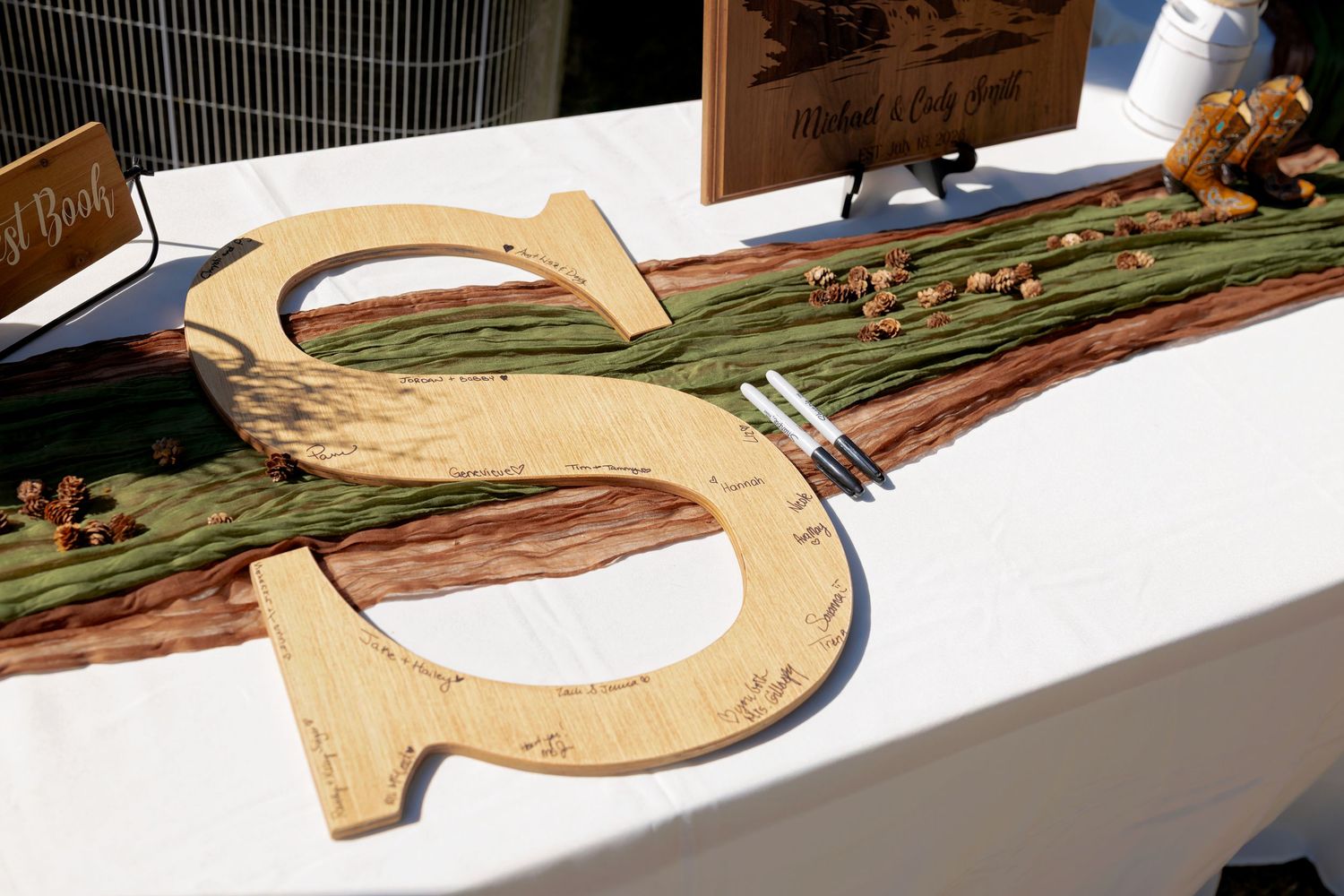 Rustic wooden letter S wedding guest book sign on white table with greenery and natural wood decor.