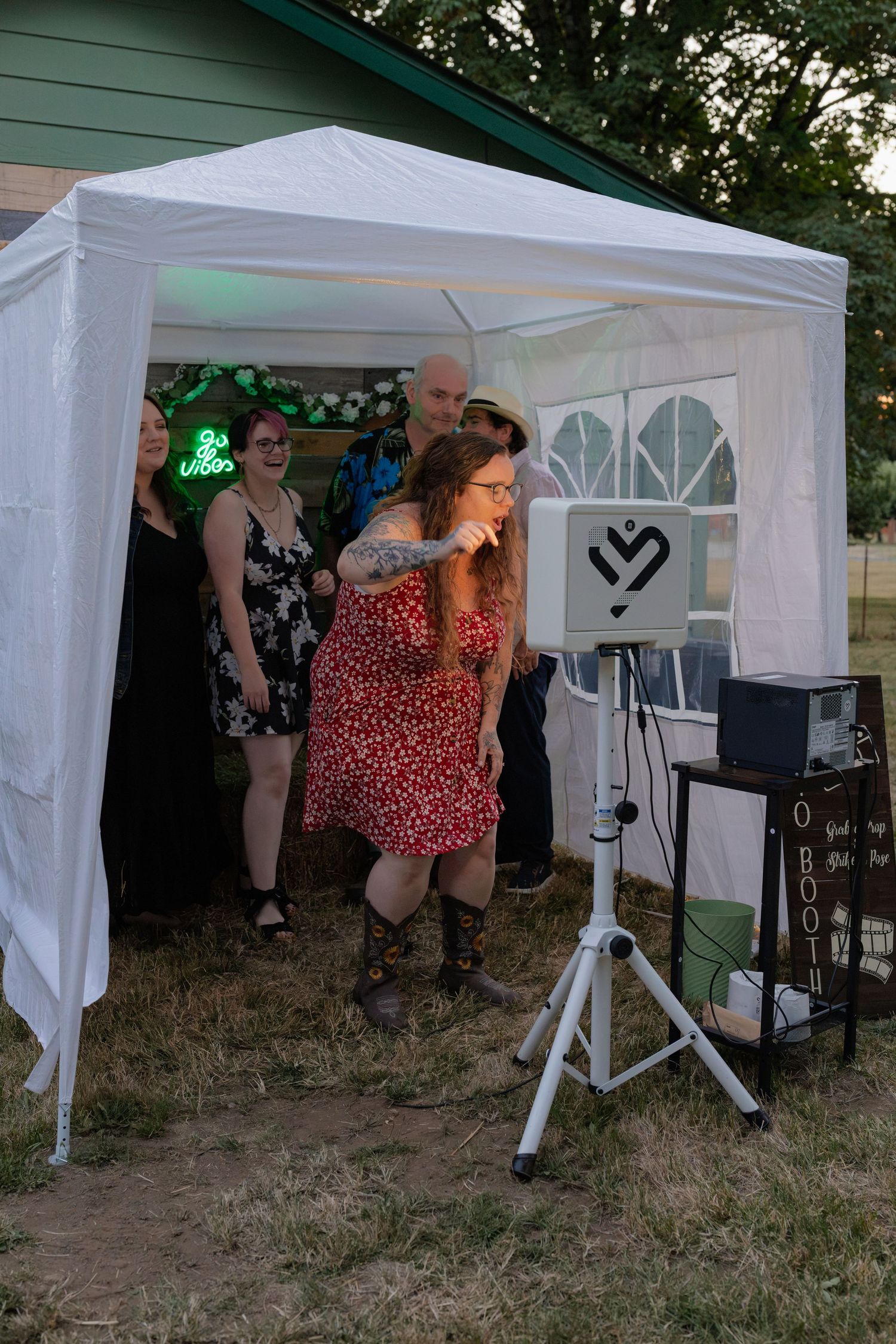 Guests enjoy an outdoor wedding photo booth under a white canopy tent at an evening reception.
