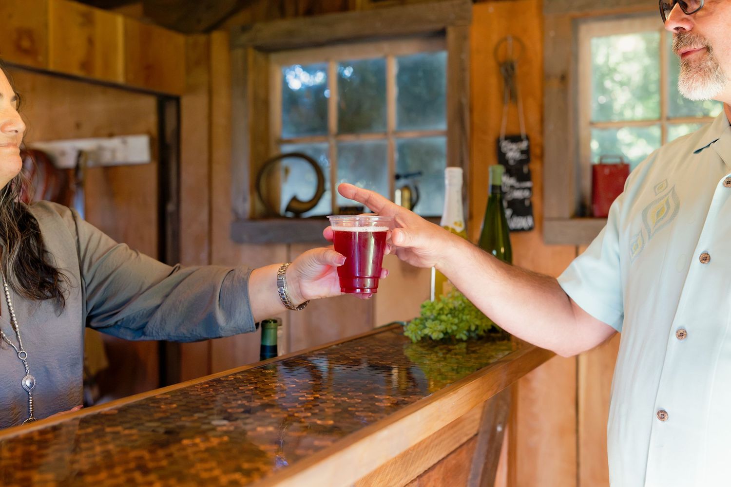 Person handing a red cup drink across a rustic wooden bar counter.