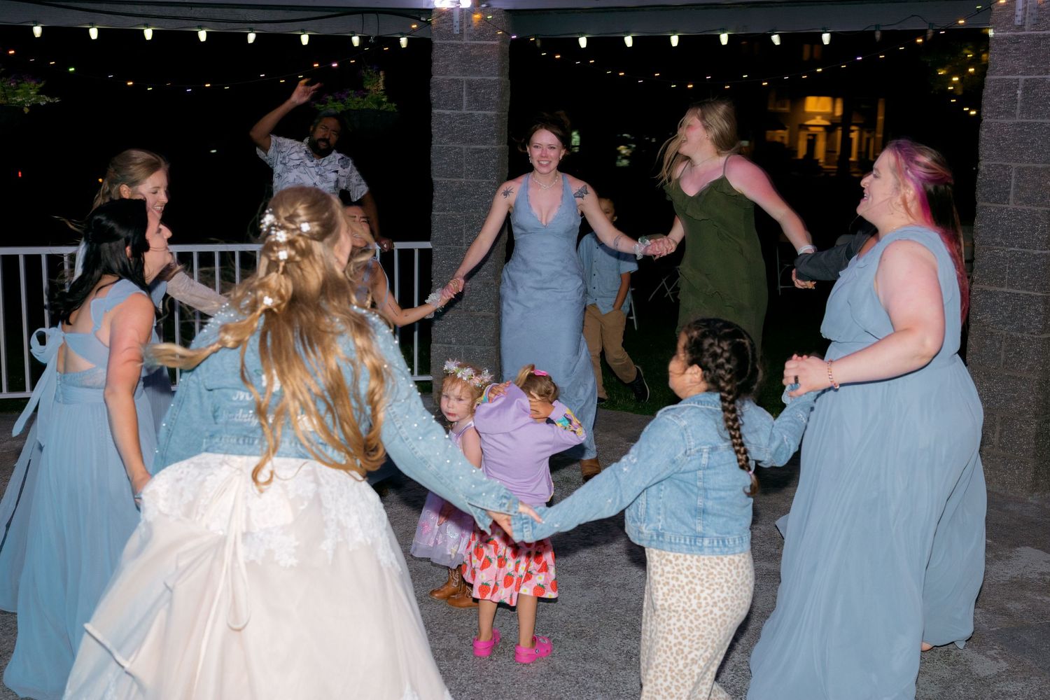 Bridesmaids in blue dresses dancing in circle with flower girl at wedding reception.