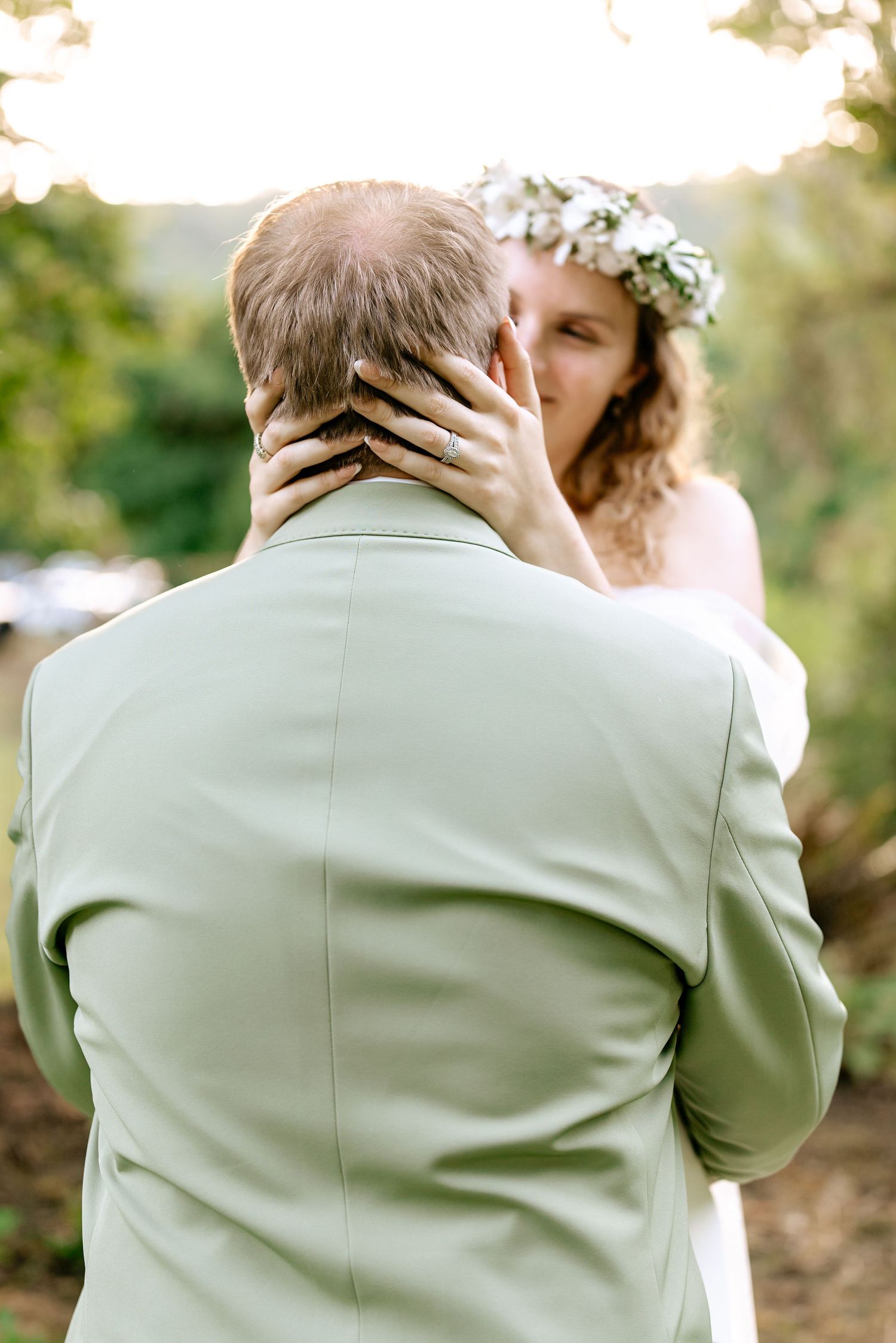 Bride in floral crown tenderly touching groom's face during outdoor wedding ceremony.