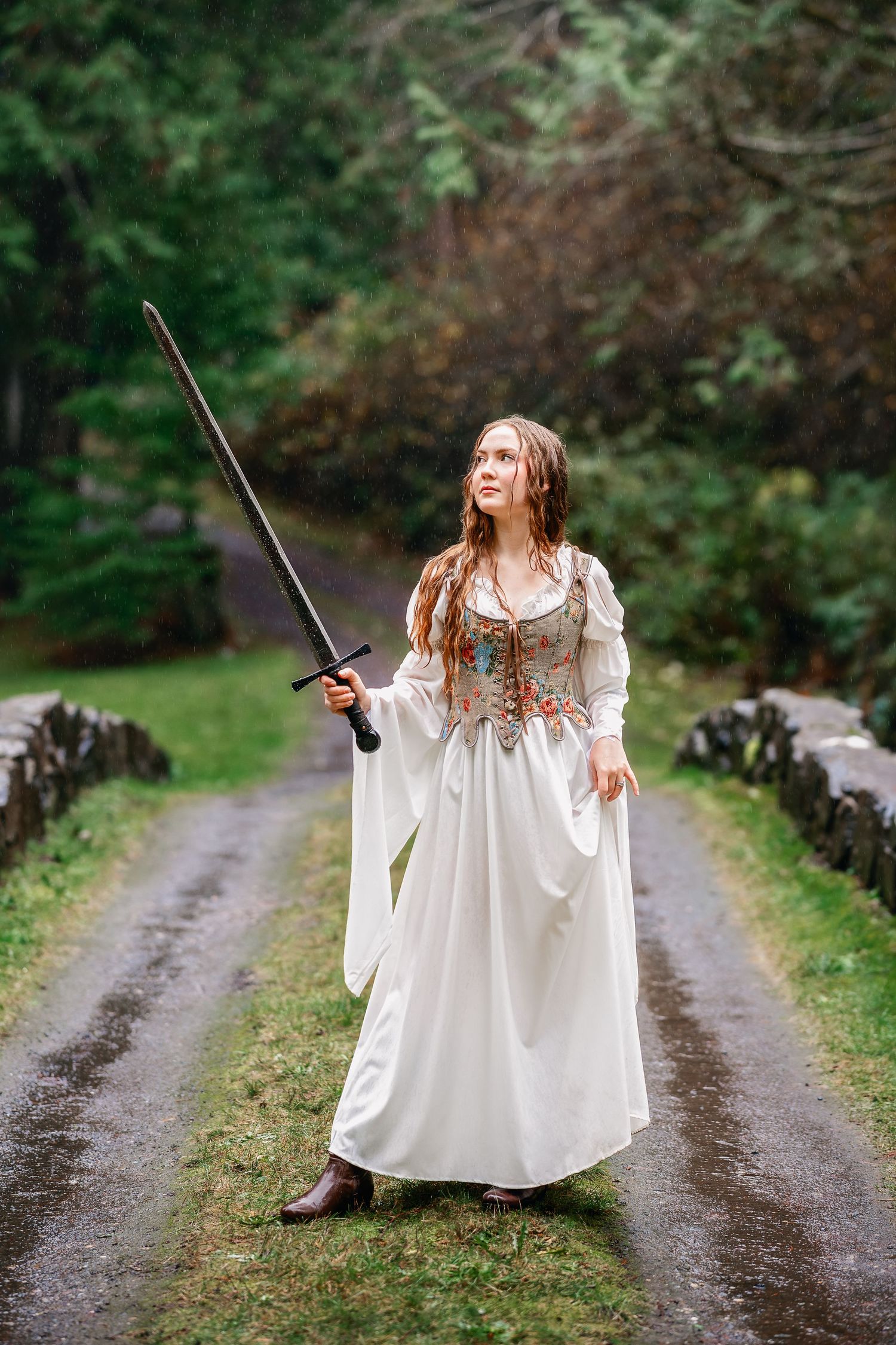 A person in a flowing white dress holds a wand while standing on a rustic dirt path.