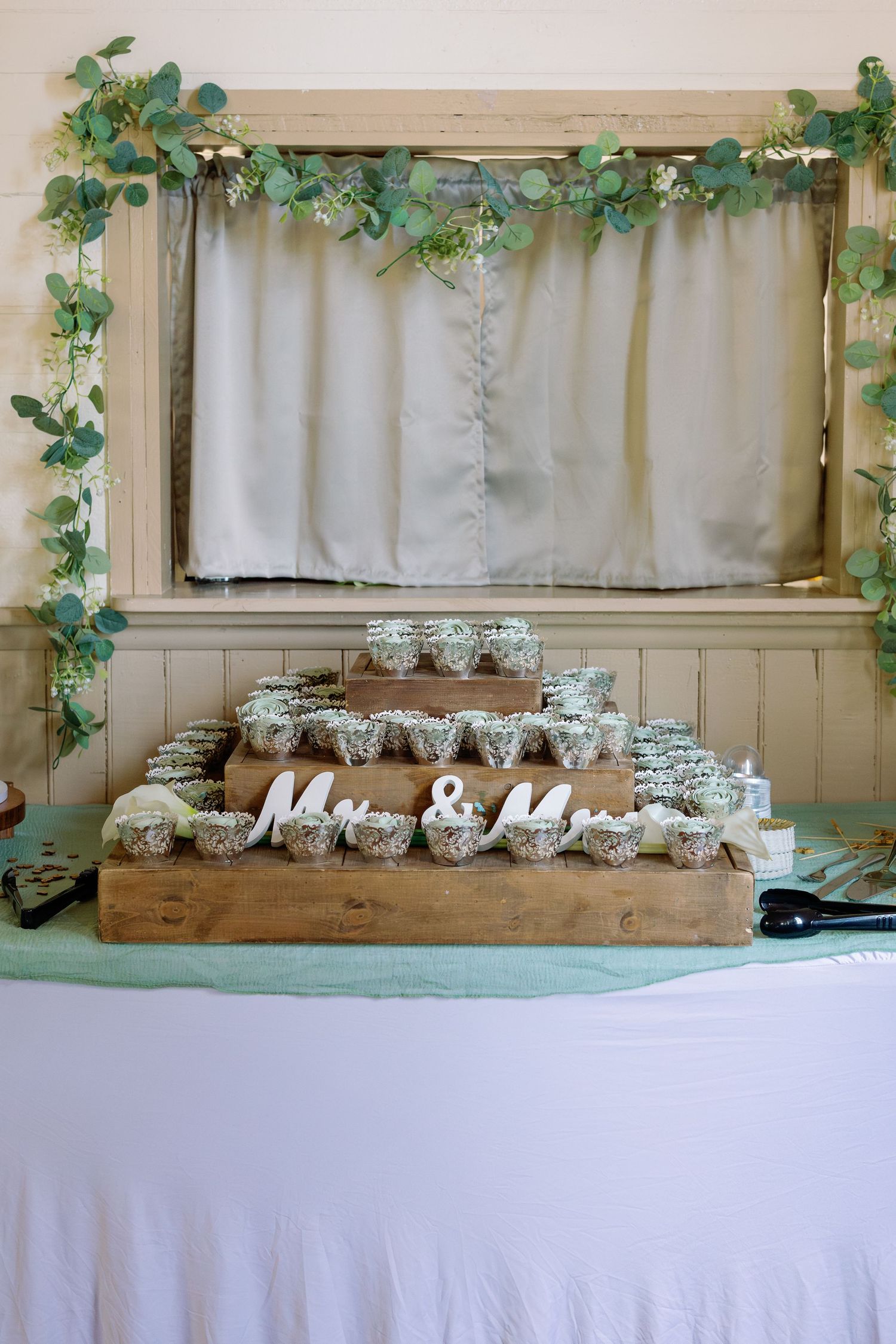 Rustic wedding display with wooden stands decorated with eucalyptus garland and Mr & Mrs signage.