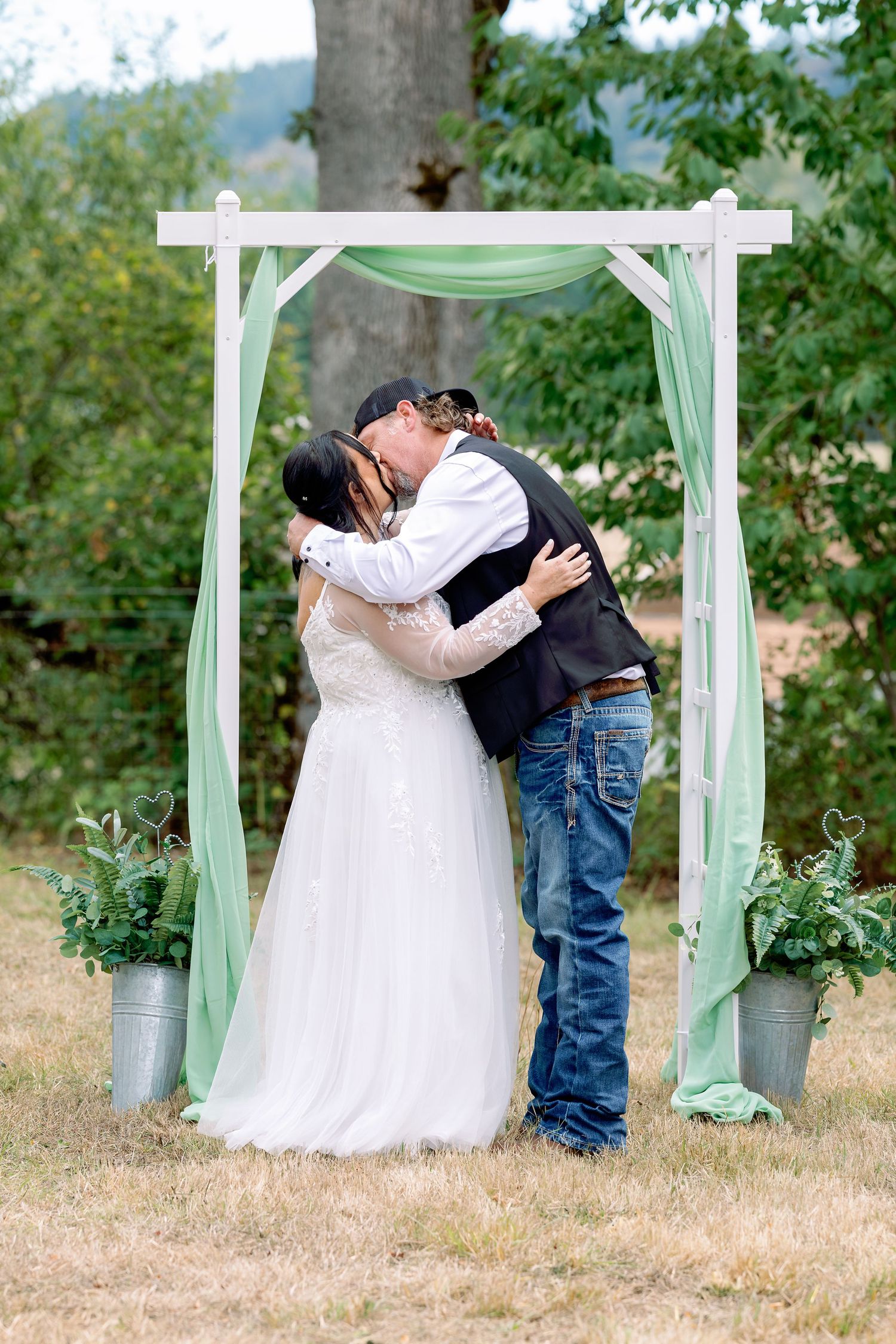 A romantic outdoor wedding scene with white arches draped in mint green fabric and floral arrangements in galvanized buckets.