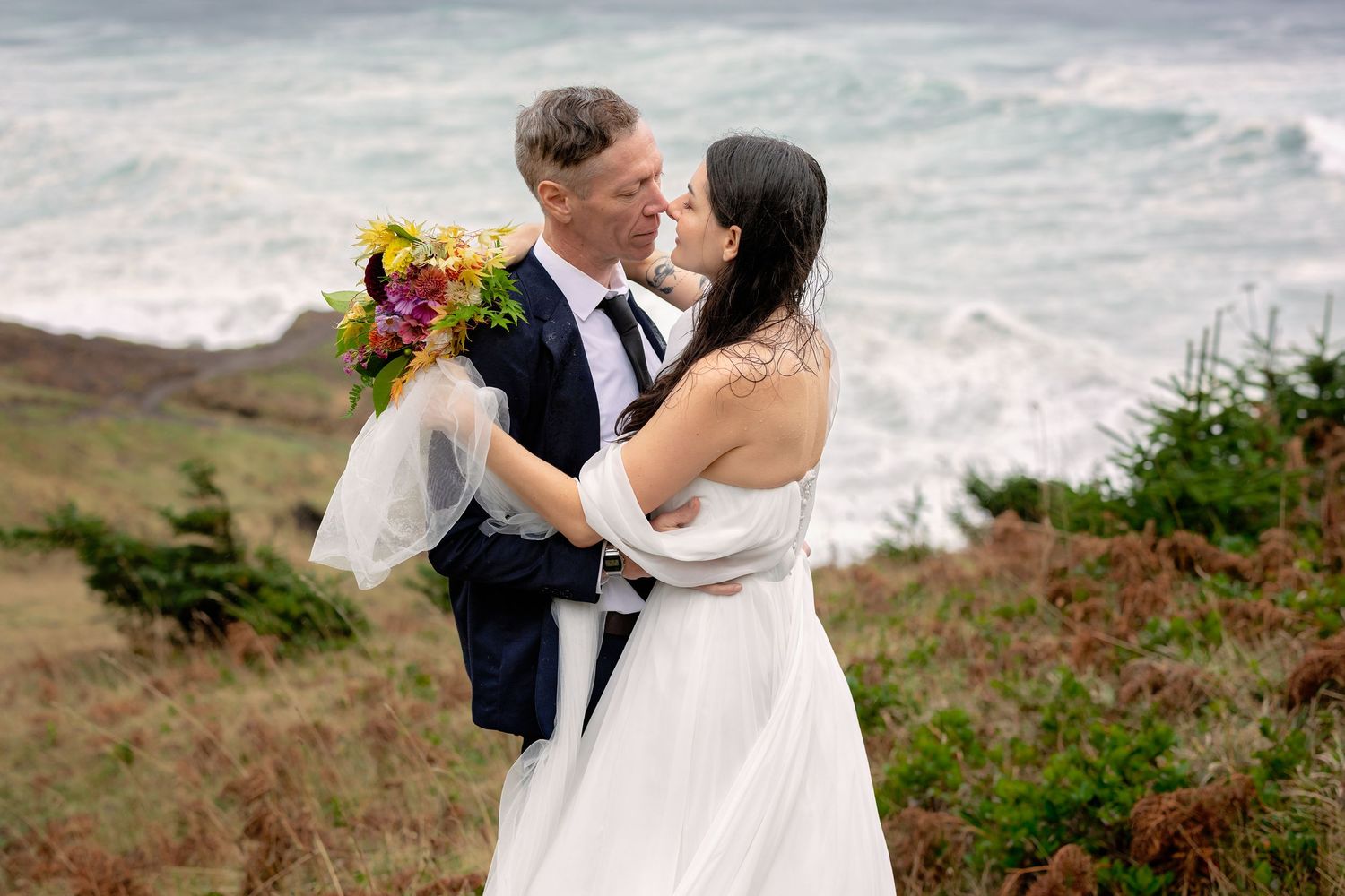 A couple shares a romantic moment on a scenic coastal cliff overlooking the ocean.