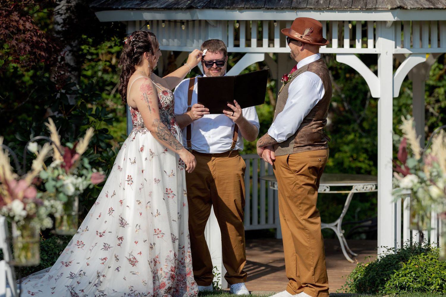 People gather outdoors near a white gazebo during a celebration with floral decorations.